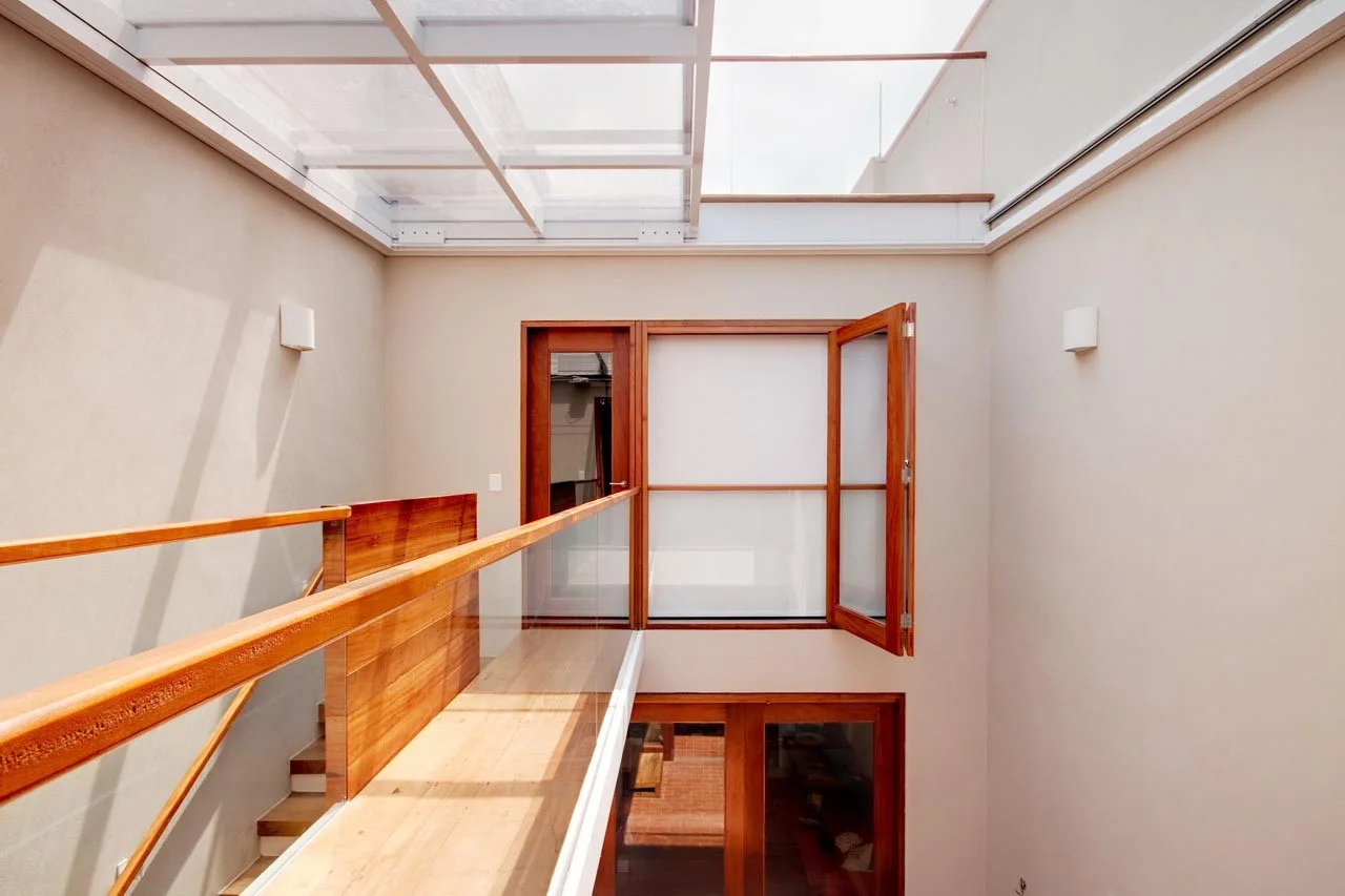 A minimalist interior landing featuring a wood and glass railing under a large overhead glass skylight with beige walls.