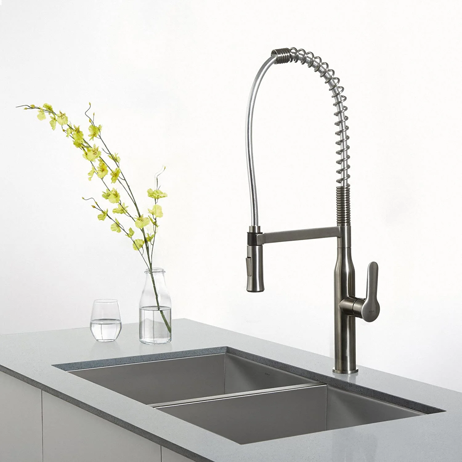 A brushed stainless steel industrial spring faucet stands over an undermount double-basin sink on a grey composite countertop.