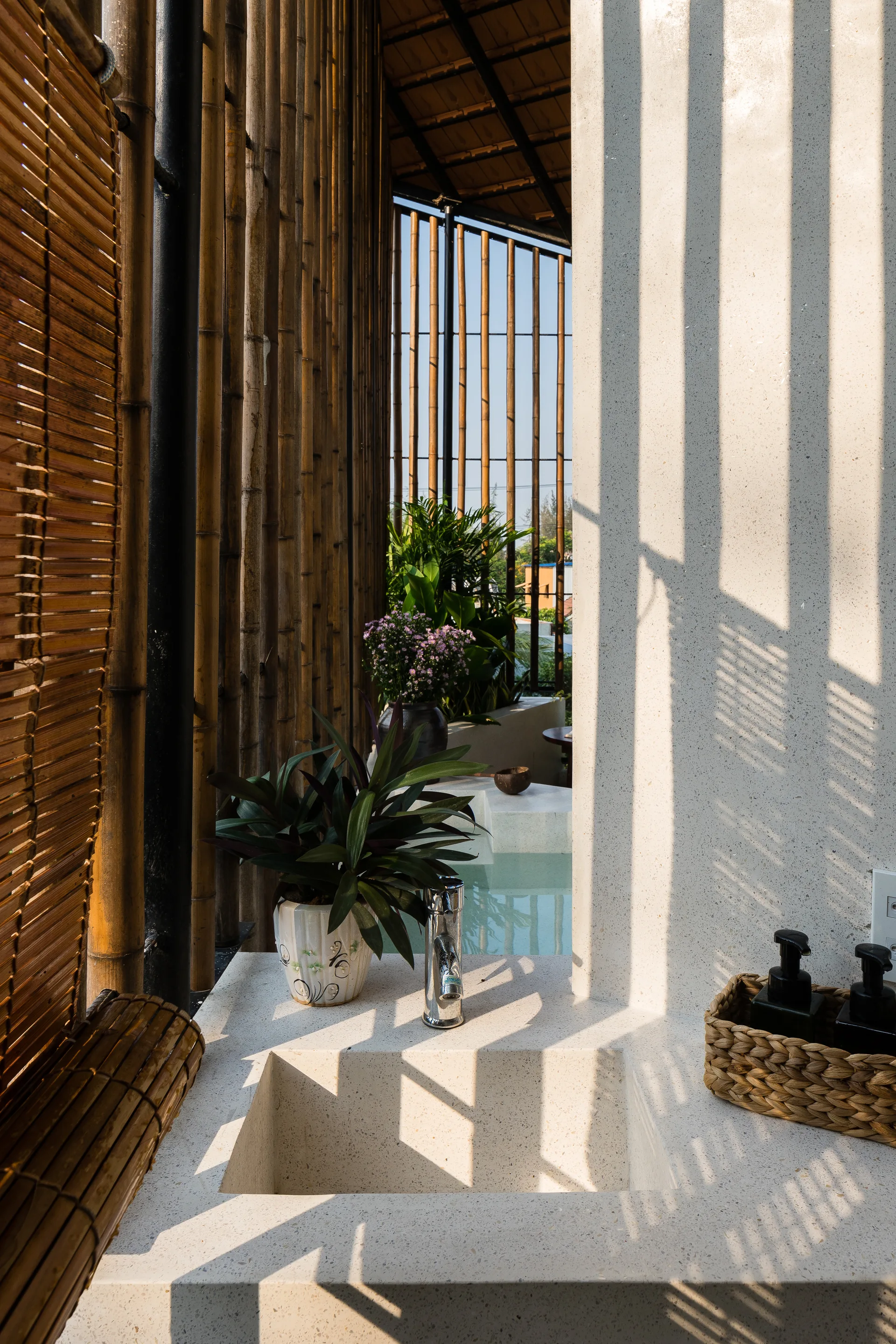 An open-air stone bathroom vanity with an integrated sink features a chrome faucet beside a tall vertical bamboo privacy screen.