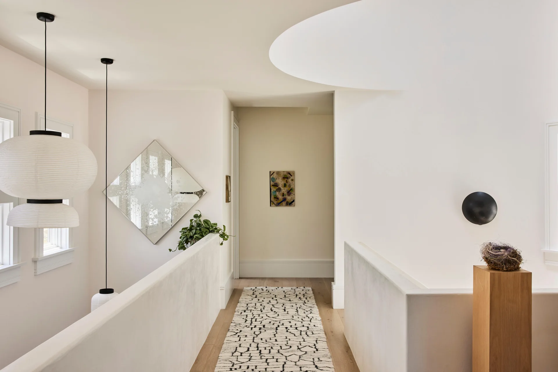 A minimalist hallway landing with off-white plaster railings, a patterned runner, and a large layered paper lantern pendant light.
