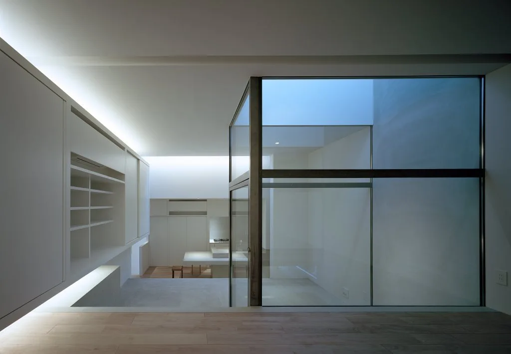 A minimalist white residential interior featuring a central glass partition, integrated cove lighting, and smooth built-in cabinetry.
