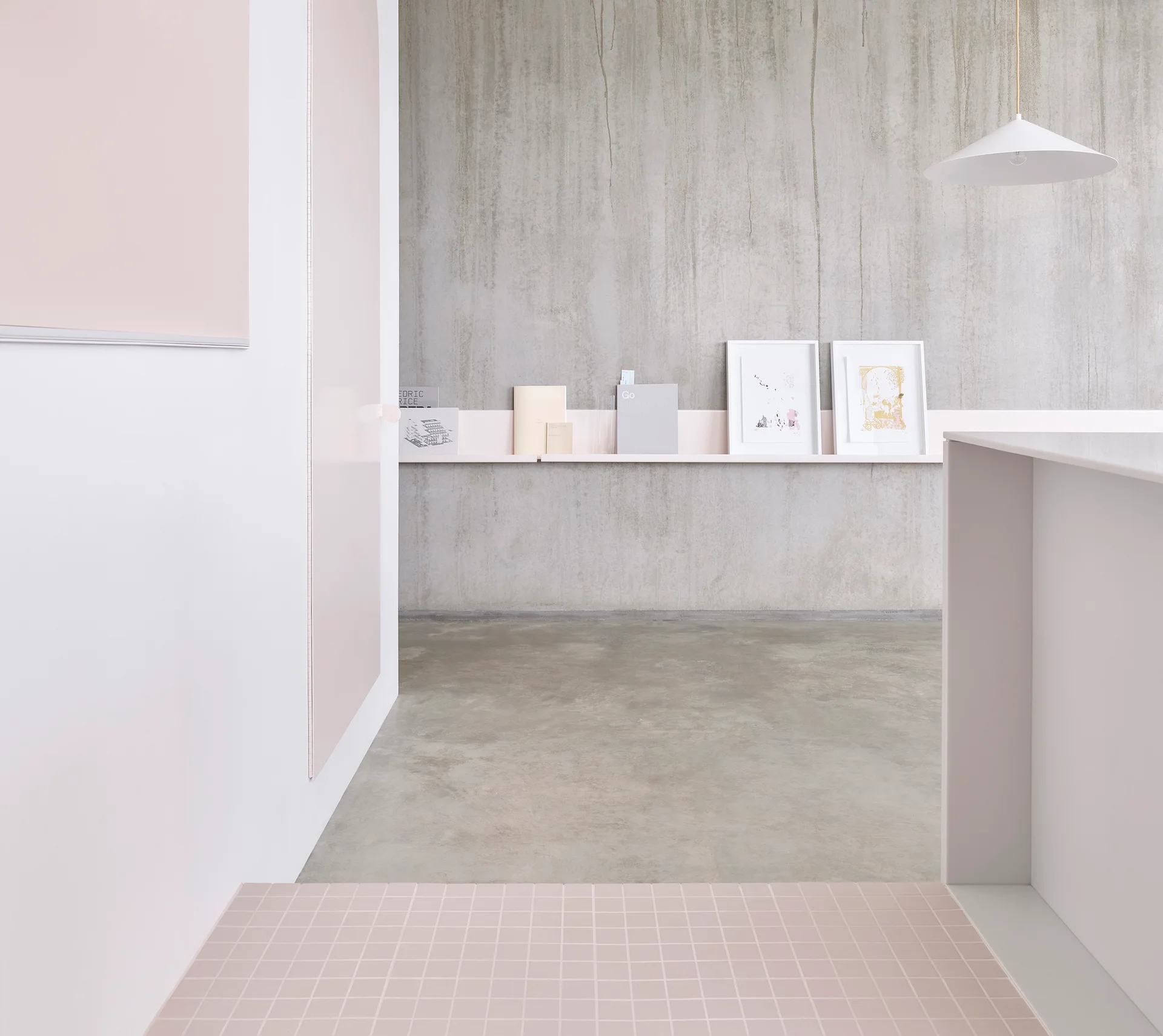 A minimalist room features a textured concrete wall with a slim pink shelf, pink grid floor tiles, and a white hanging pendant light.