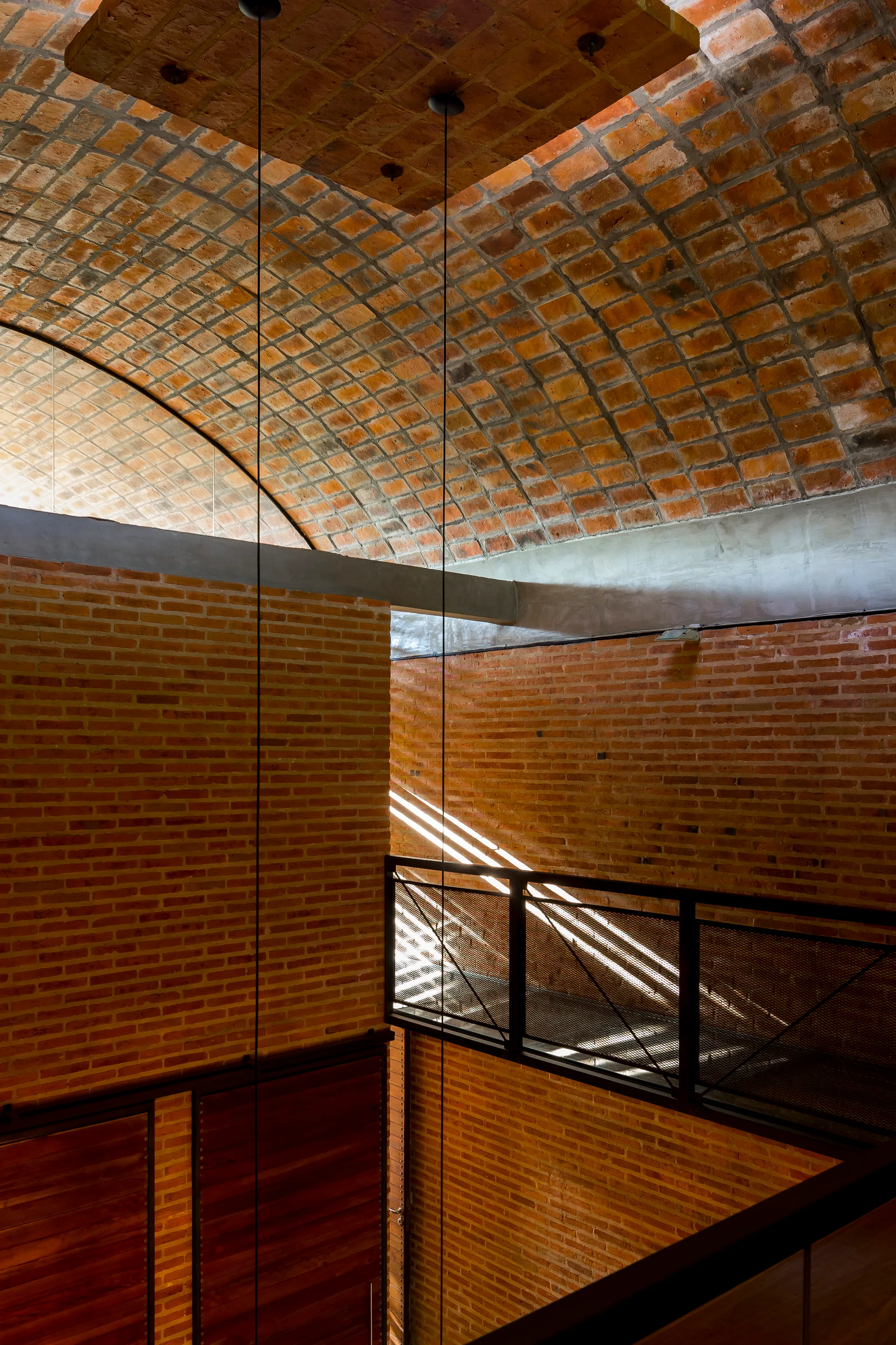 An industrial interior features a curved red brick barrel vault ceiling, exposed brick walls, and a black metal mesh mezzanine walkway.