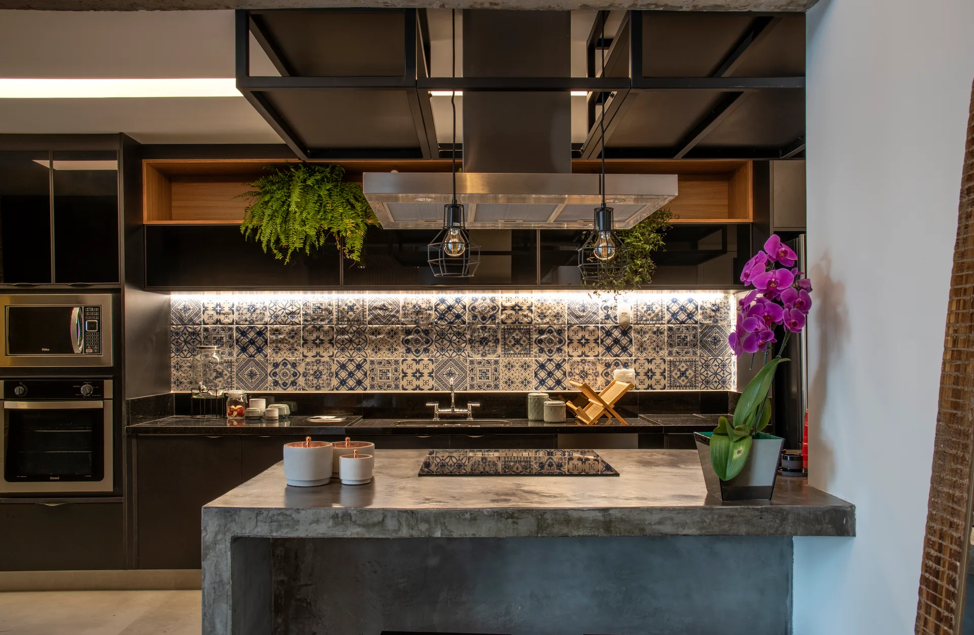 A modern industrial kitchen features a textured concrete island, matte black cabinets, and a blue and white patterned tile backsplash.