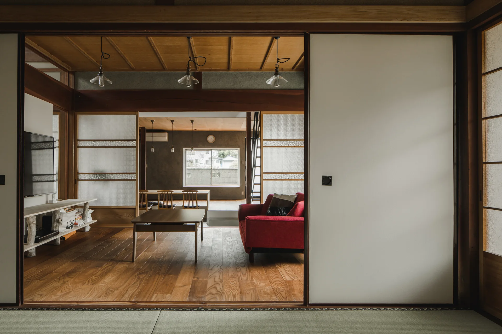 Traditional Japanese-style living room with a red sofa, a low wooden coffee table, sliding shoji screen doors, and tatami mats in the foreground.