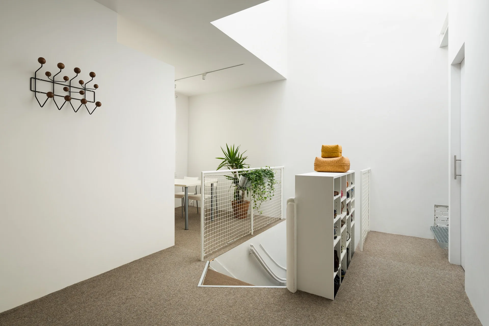 A minimalist white staircase landing with a metal grid safety railing, carpeted floor, and natural light from a skylight.