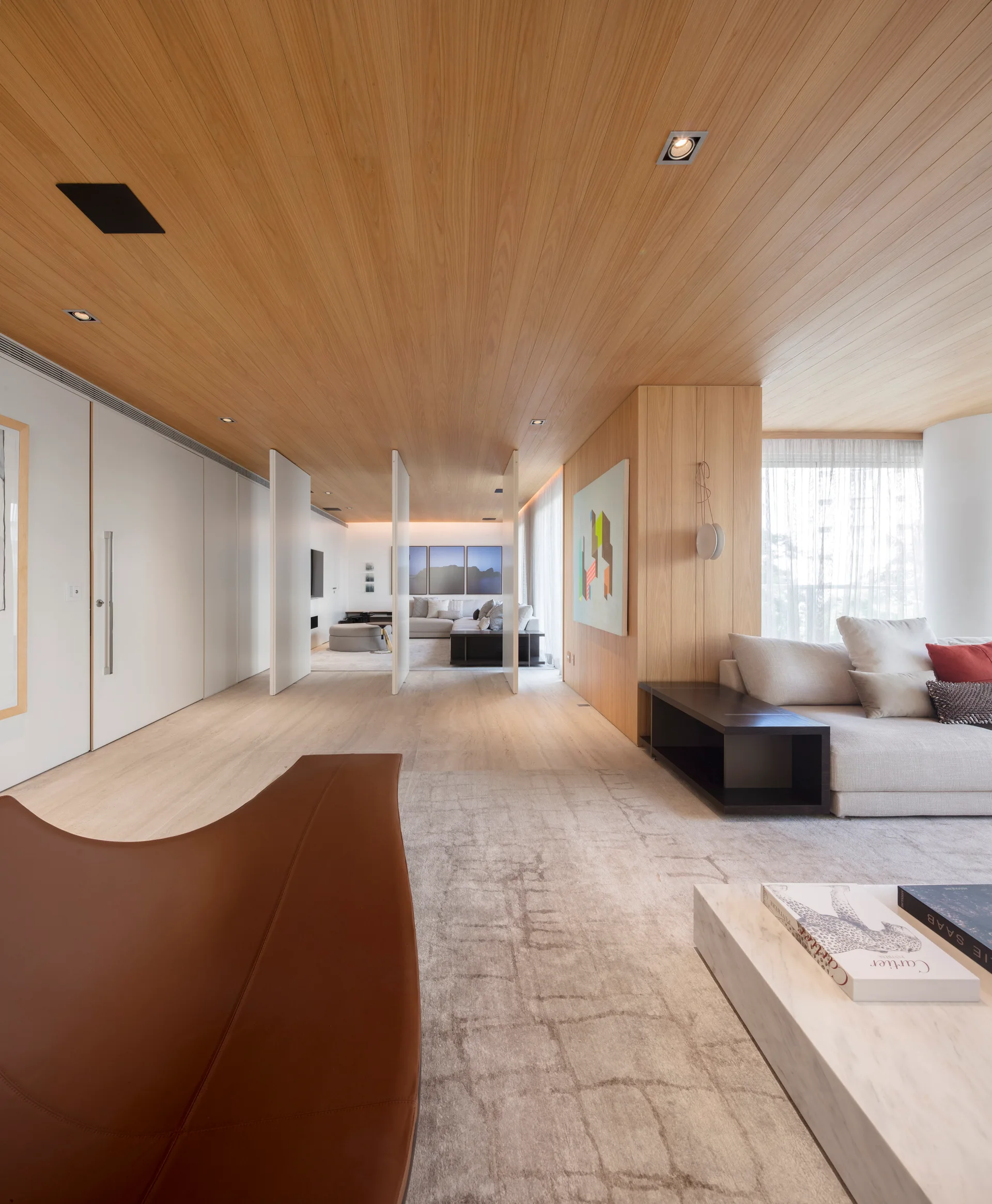 A modern living room features a wood plank ceiling, a low marble coffee table, beige sofas, and pivoting white partition panels.