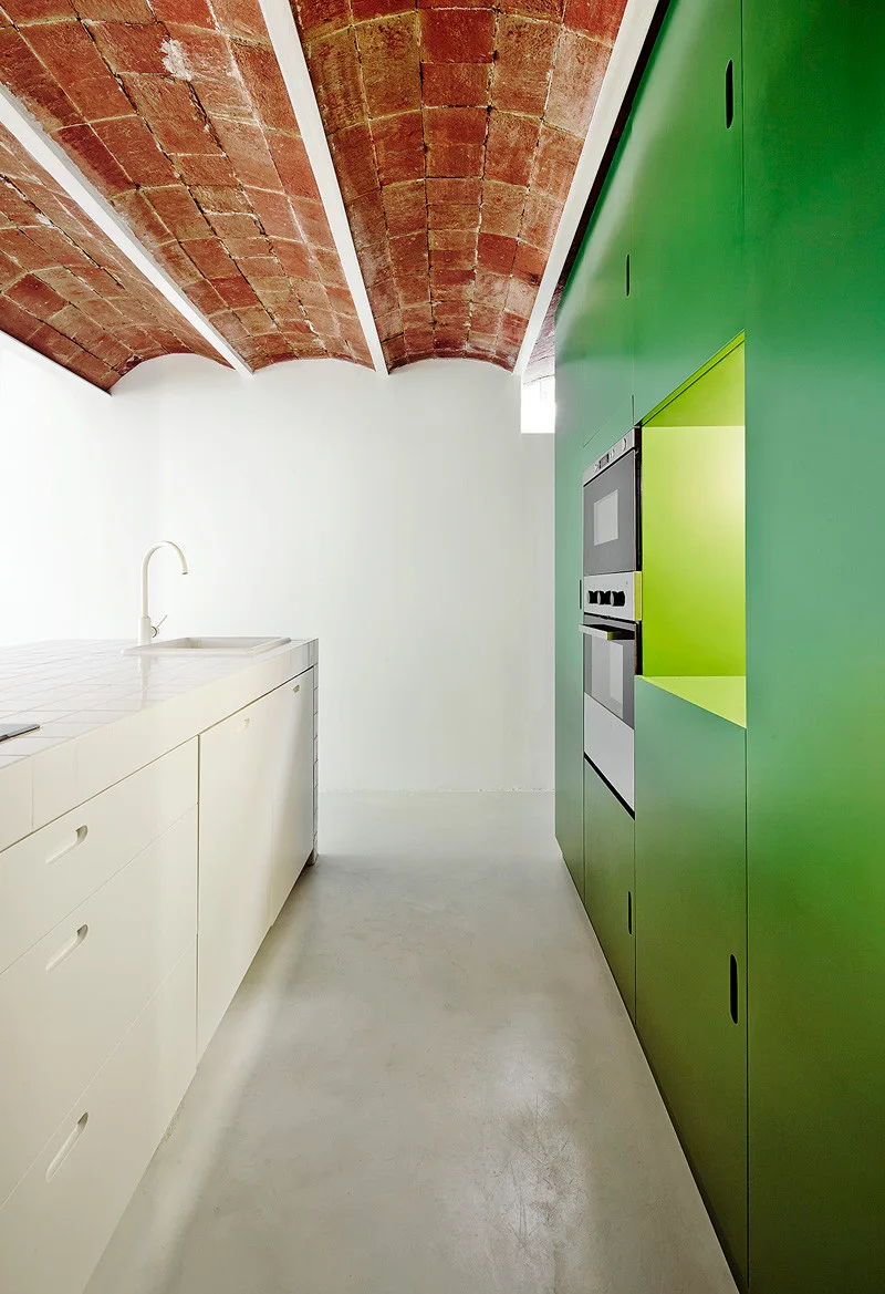 A minimalist kitchen featuring a tiled island, tall green cabinets with a built-in oven, and a red brick vaulted ceiling.