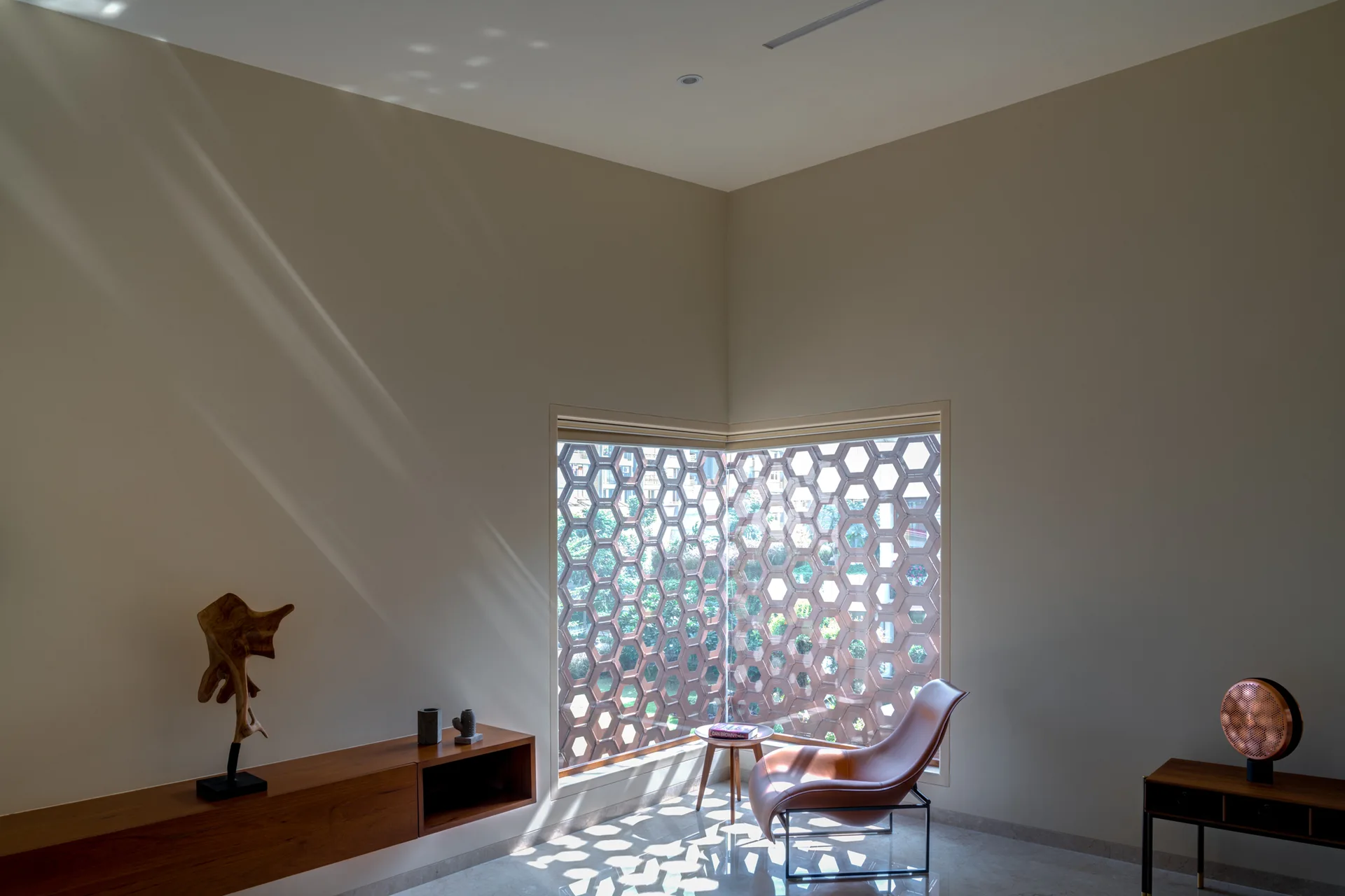 A leather lounge chair rests near a corner window featuring a terracotta honeycomb lattice screen that casts geometric shadows on the floor.