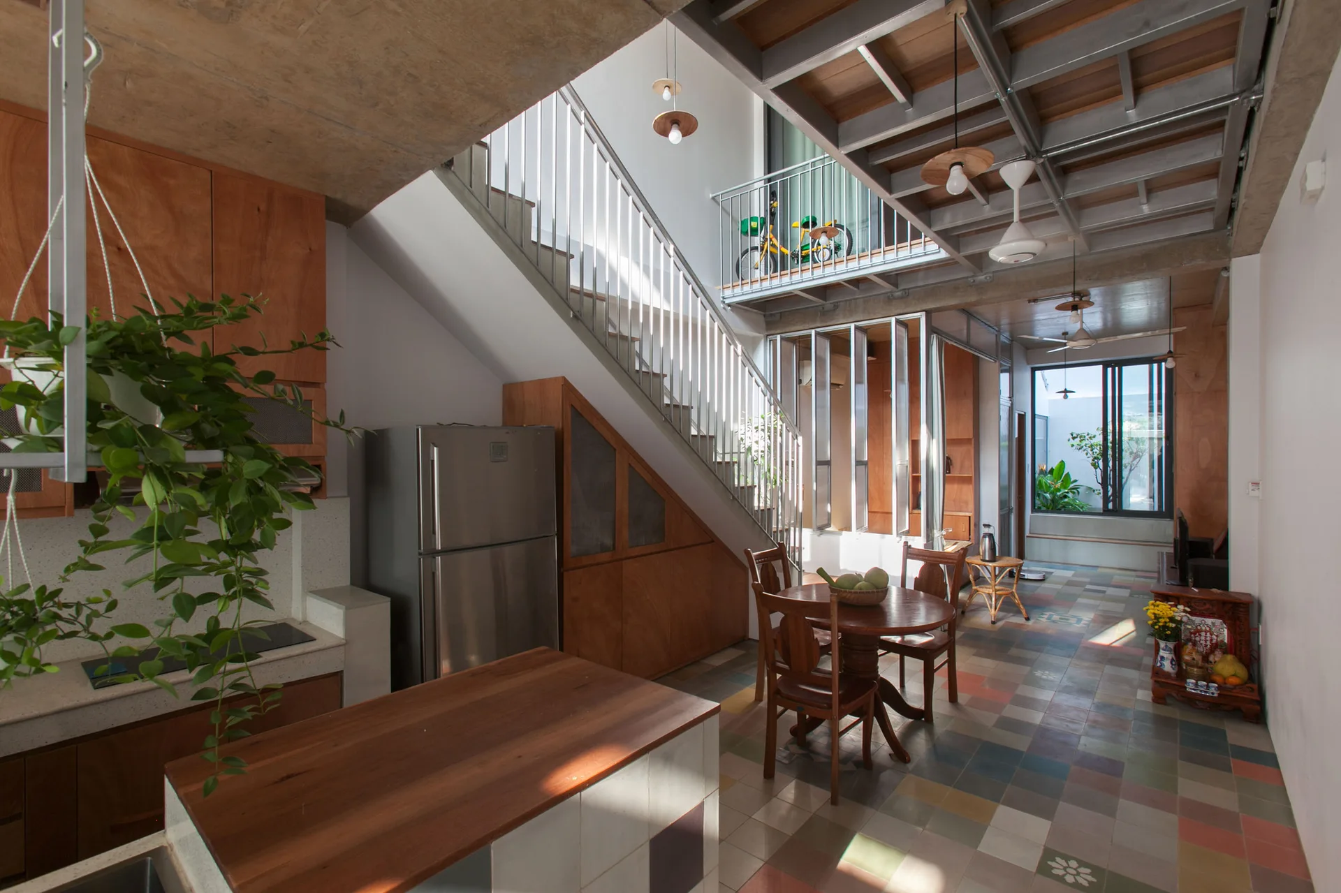 An open-plan kitchen and dining space features a metal staircase, wood cabinetry under the stairs, and a colorful patterned tile floor.