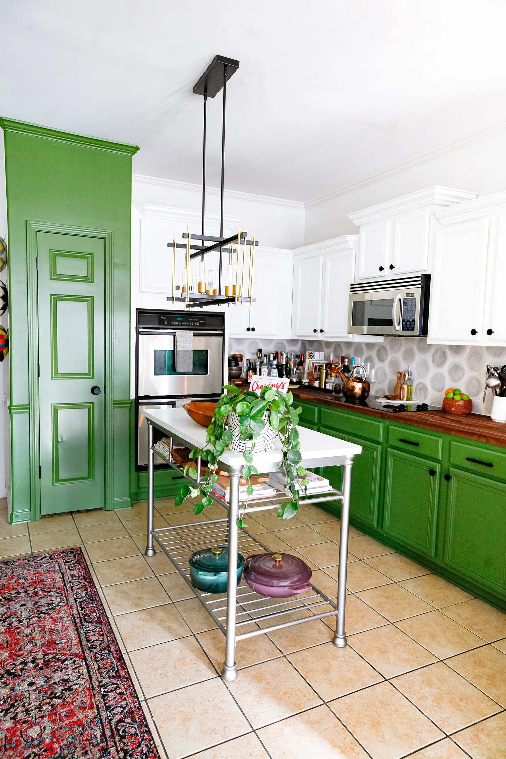 A kitchen featuring green lower cabinets, white upper cabinets, a hexagonal tile backsplash, and a central metal island.