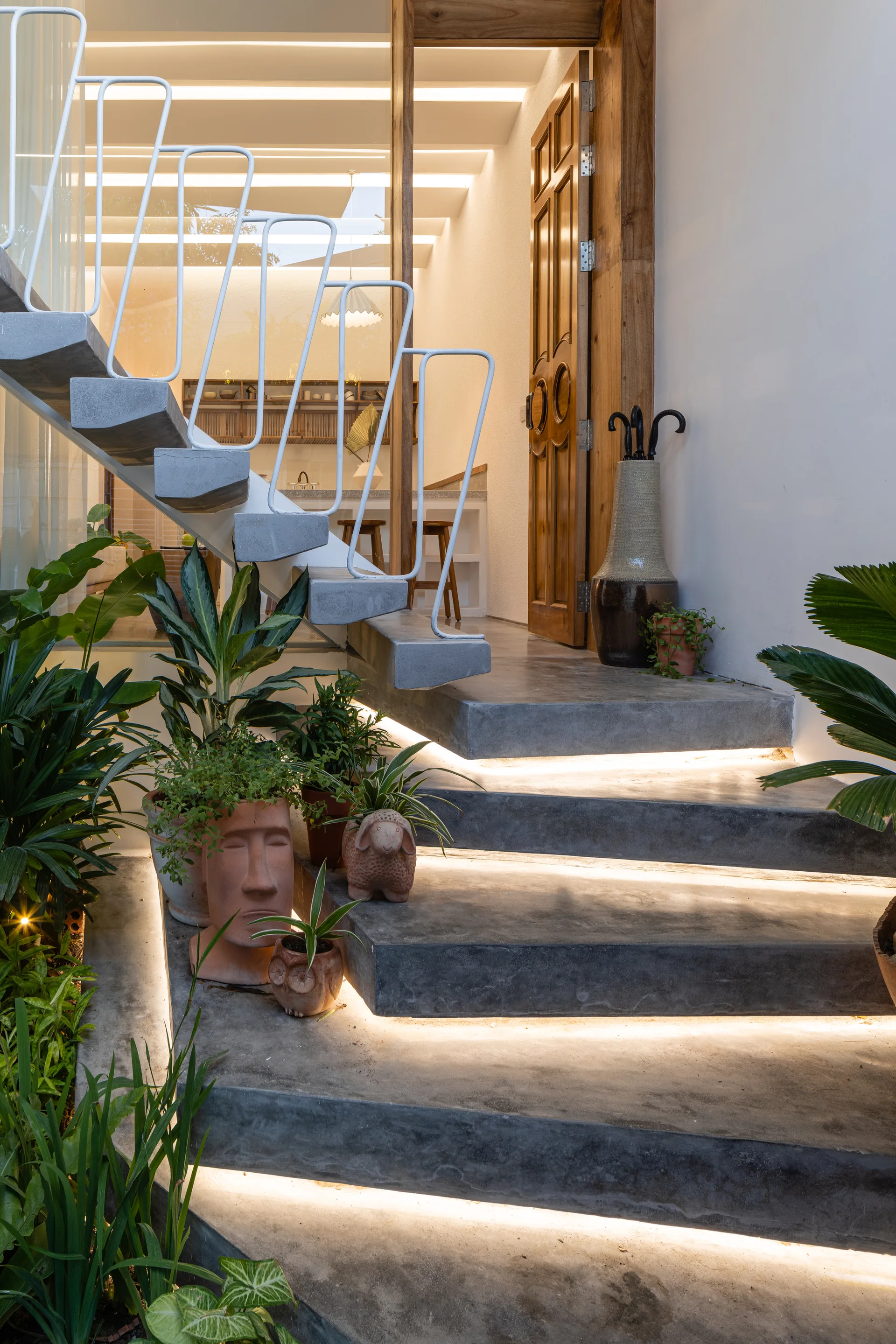 A modern concrete staircase featuring floating treads illuminated by warm LED strip lights, styled with potted plants next to a white metal railing.