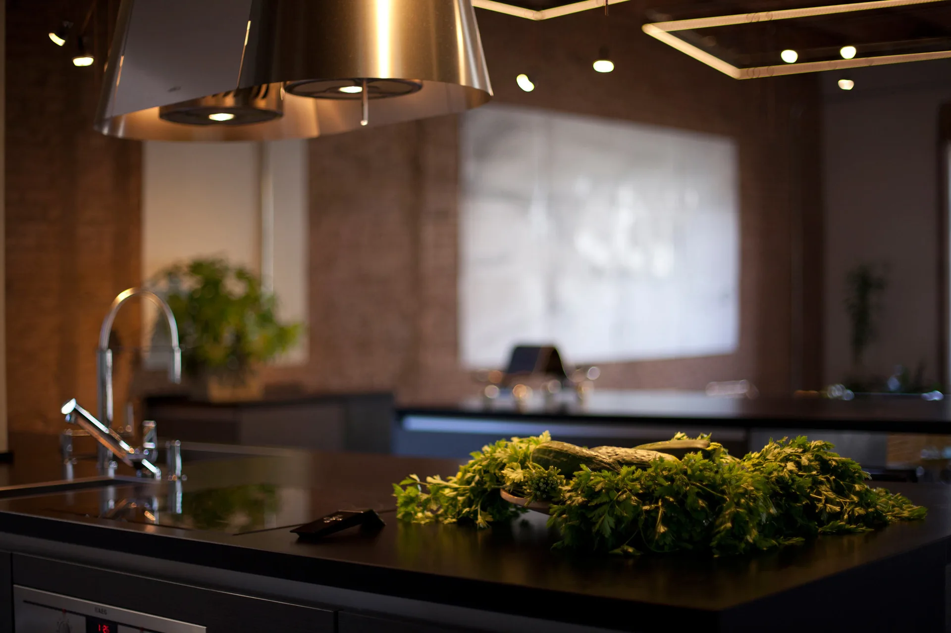 A contemporary kitchen island with a matte black countertop, integrated sink, and stainless steel range hood set against a warm exposed brick wall.