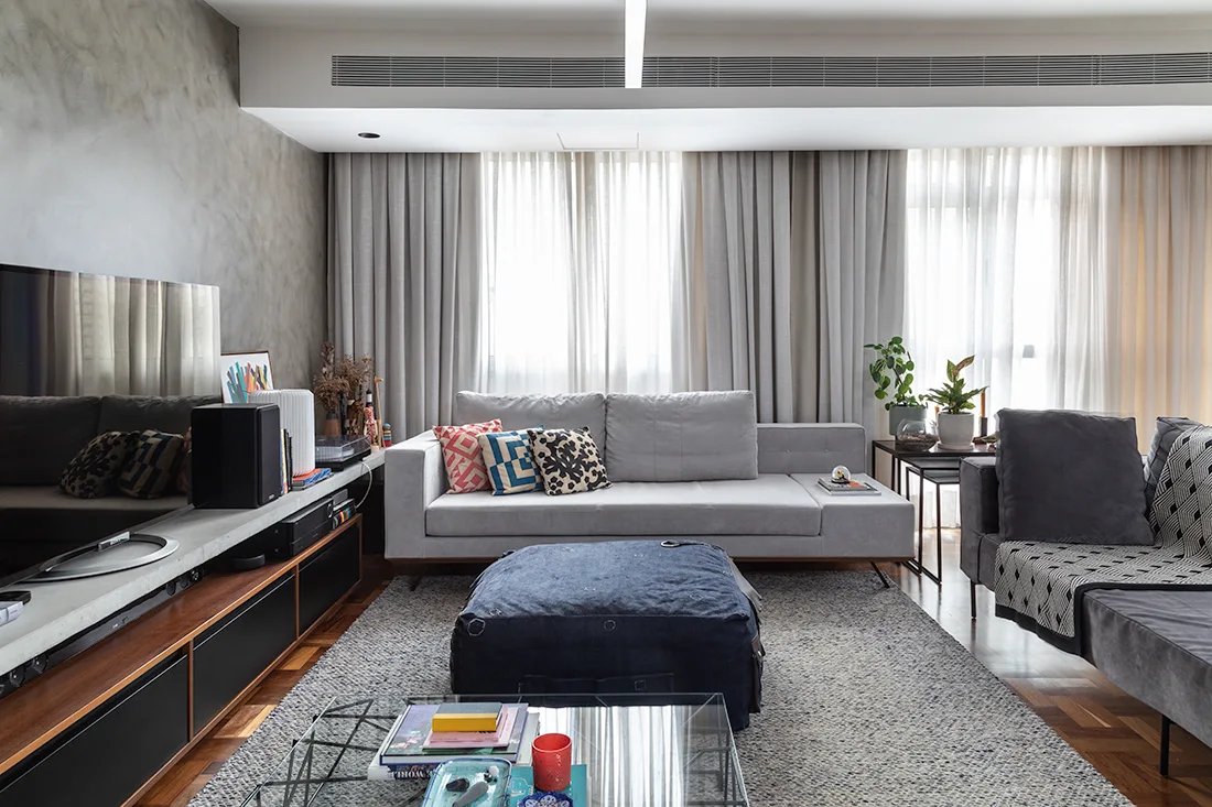 A modern living room features a light gray sofa, a blue ottoman, and a low wooden media console against a textured concrete accent wall.