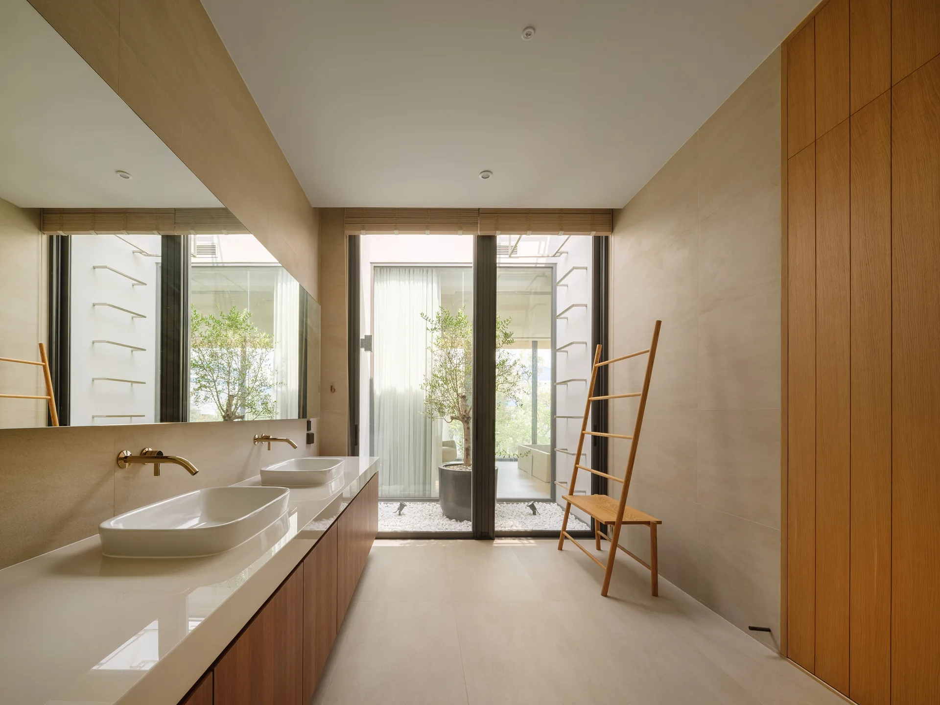 Minimalist bathroom with a floating wood vanity, dual sinks, large mirror, and a sliding glass door opening to an outdoor courtyard.