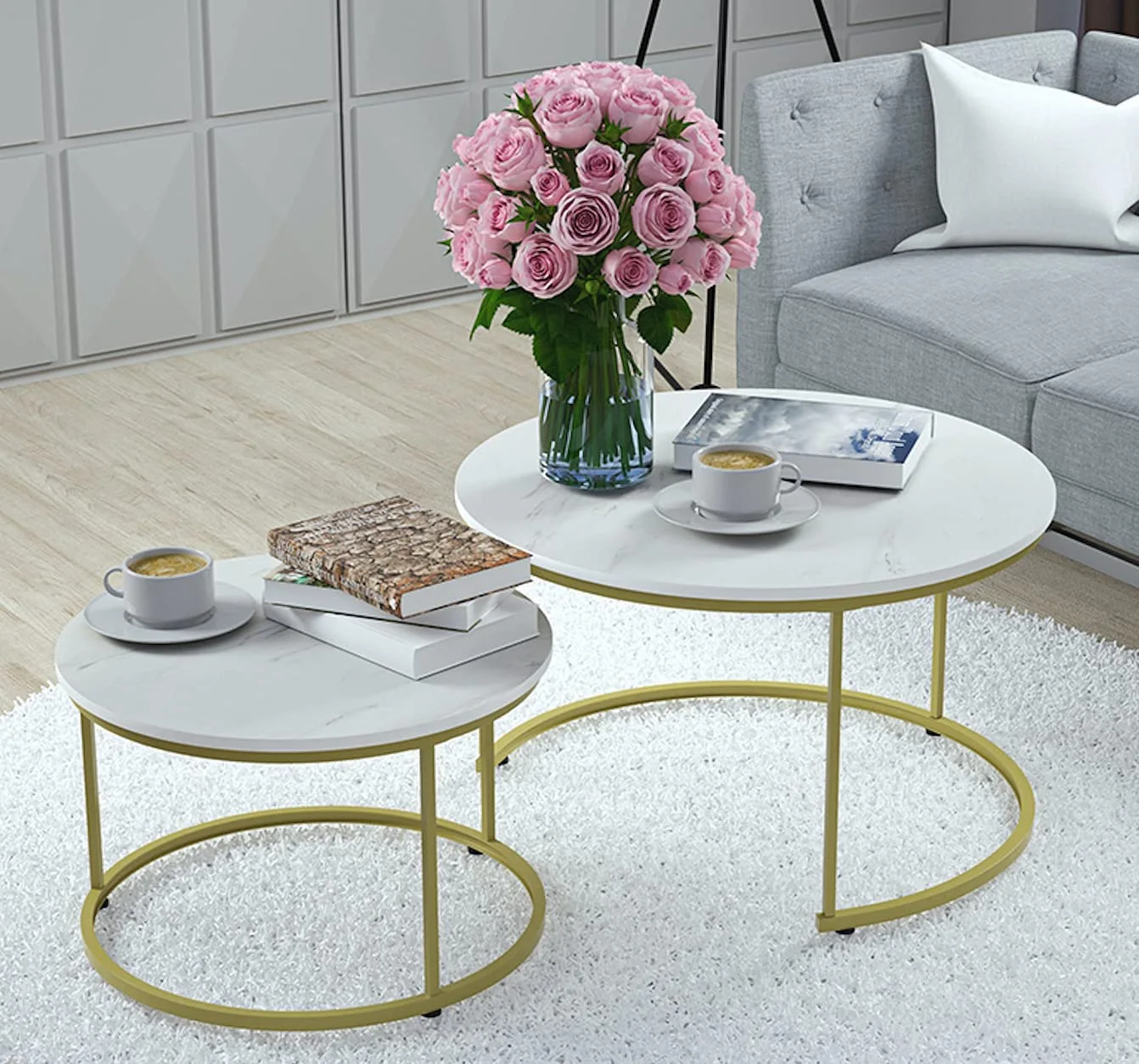 Two round nesting coffee tables with white marble tops and gold frames sit on a white shag rug next to a grey sofa.