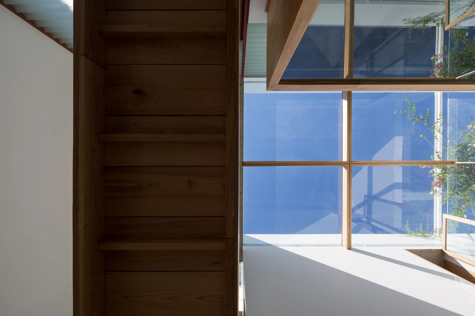 A low-angle shot looking up at a wooden staircase next to a large glass skylight revealing a bright blue sky.