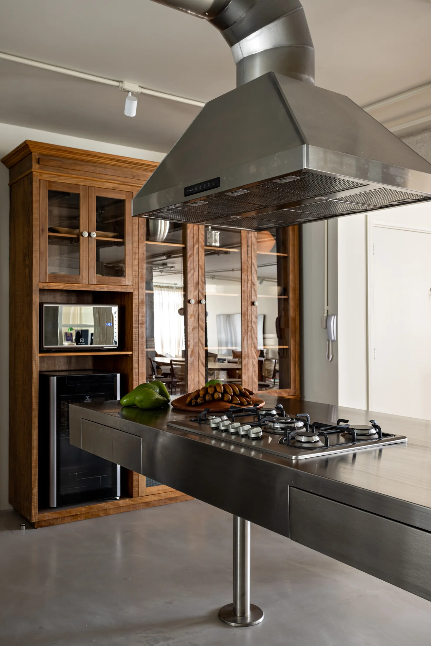 A modern kitchen with a stainless steel island, a gas cooktop under a large metal range hood, and warm wood cabinetry.