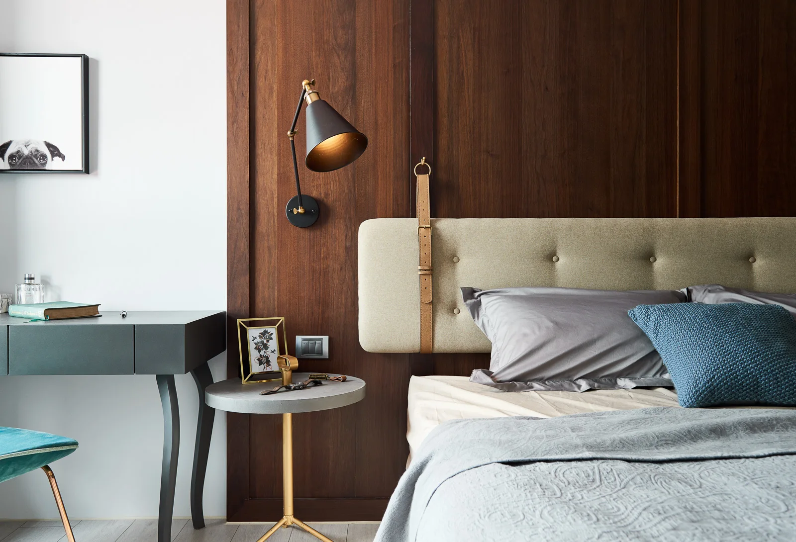 A modern bedroom sleeping area featuring a tufted upholstered headboard with leather straps against a vertical dark wood paneled wall.