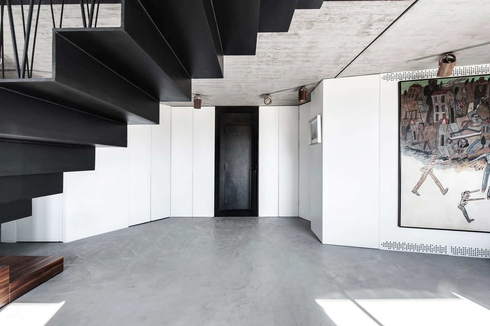 A minimalist entryway features a black metal cantilevered staircase, raw concrete floor and ceiling, and white wall cabinetry with a black door.