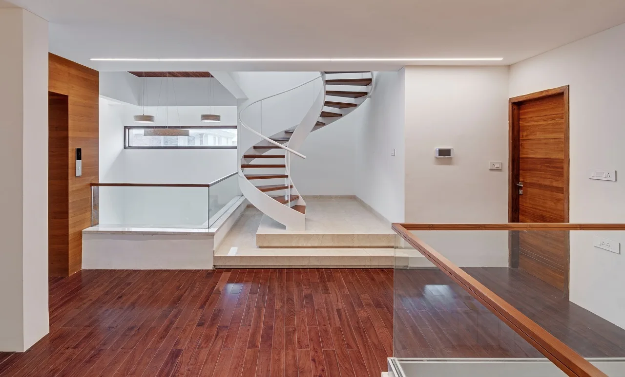 A modern hallway landing features a central white spiral staircase with wood treads, a glass railing, and dark hardwood floors.