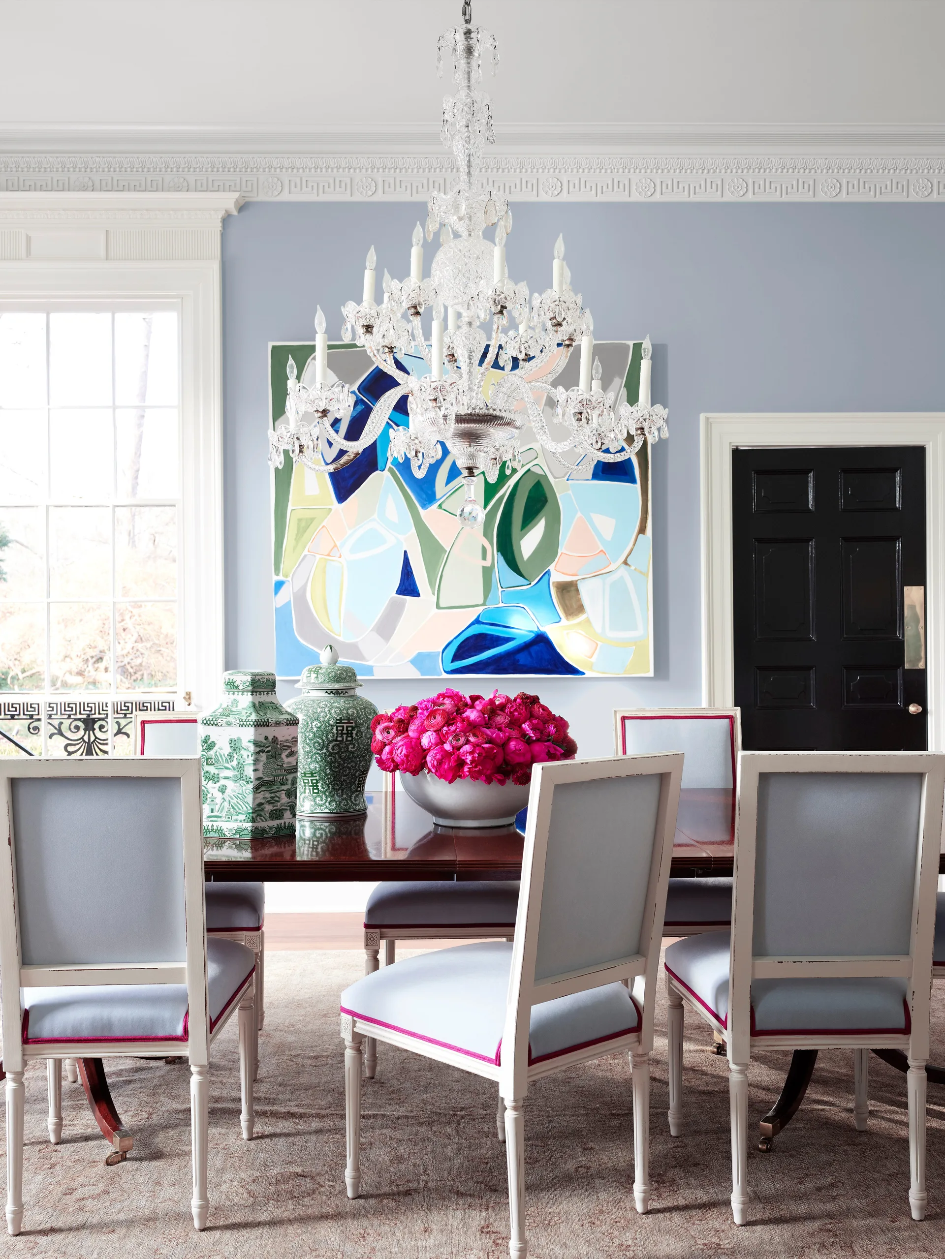 A formal dining room features light blue upholstered chairs with pink trim around a dark wood table beneath a large crystal chandelier.