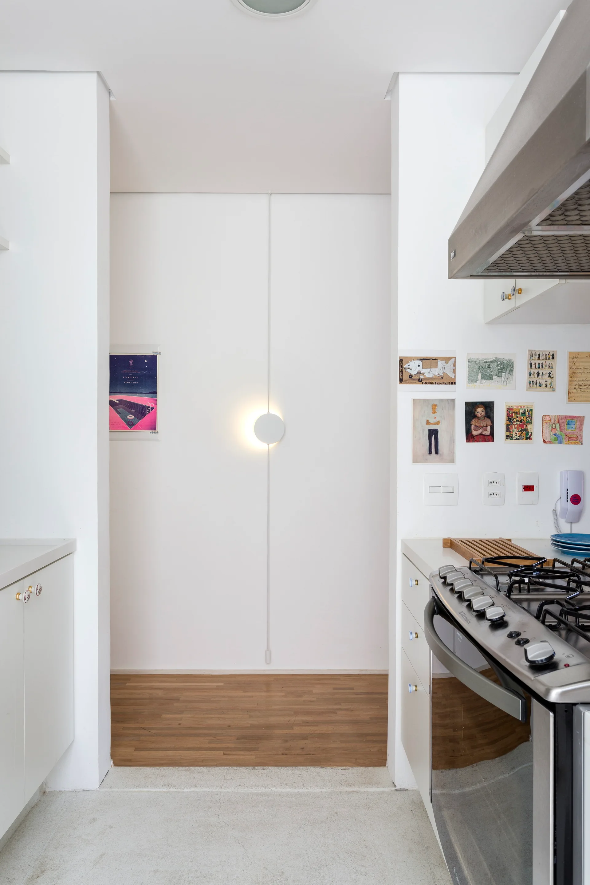 A kitchen passageway with white walls, a stainless steel stove, and a minimalist round wall light with a straight vertical cord.