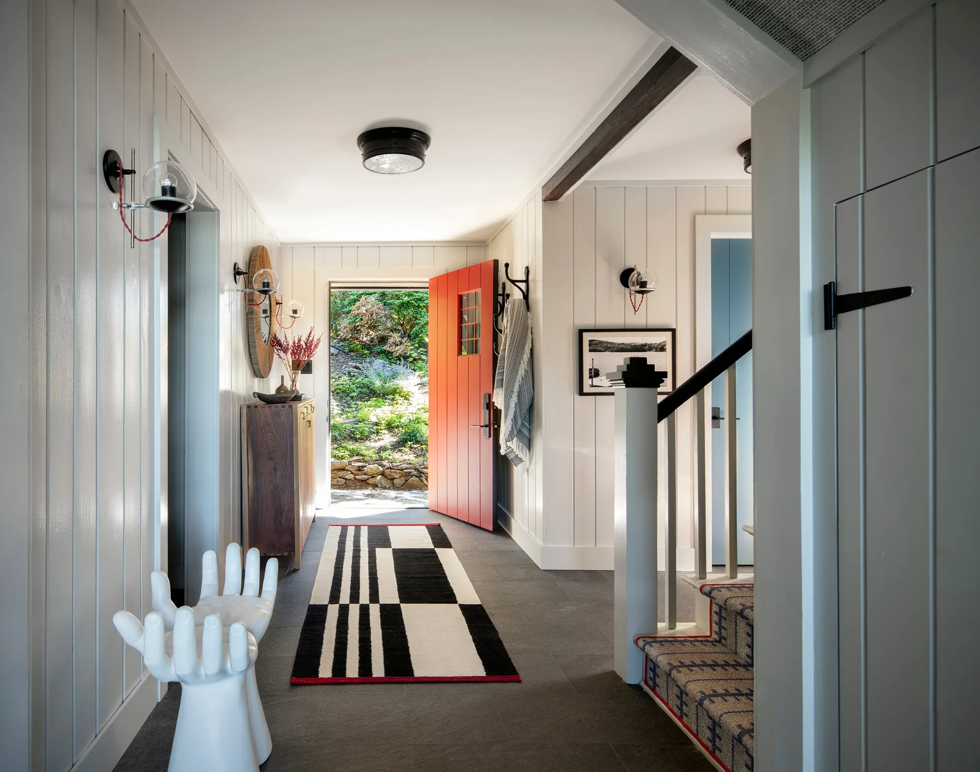 A modern entryway features painted white wall paneling, a vibrant red front door, and a geometric black and white runner rug.