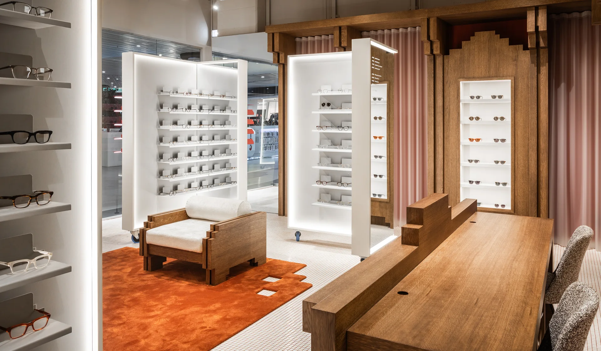 A modern retail interior with illuminated eyewear displays, a geometric wooden armchair on a bright orange rug, and a large wooden counter.