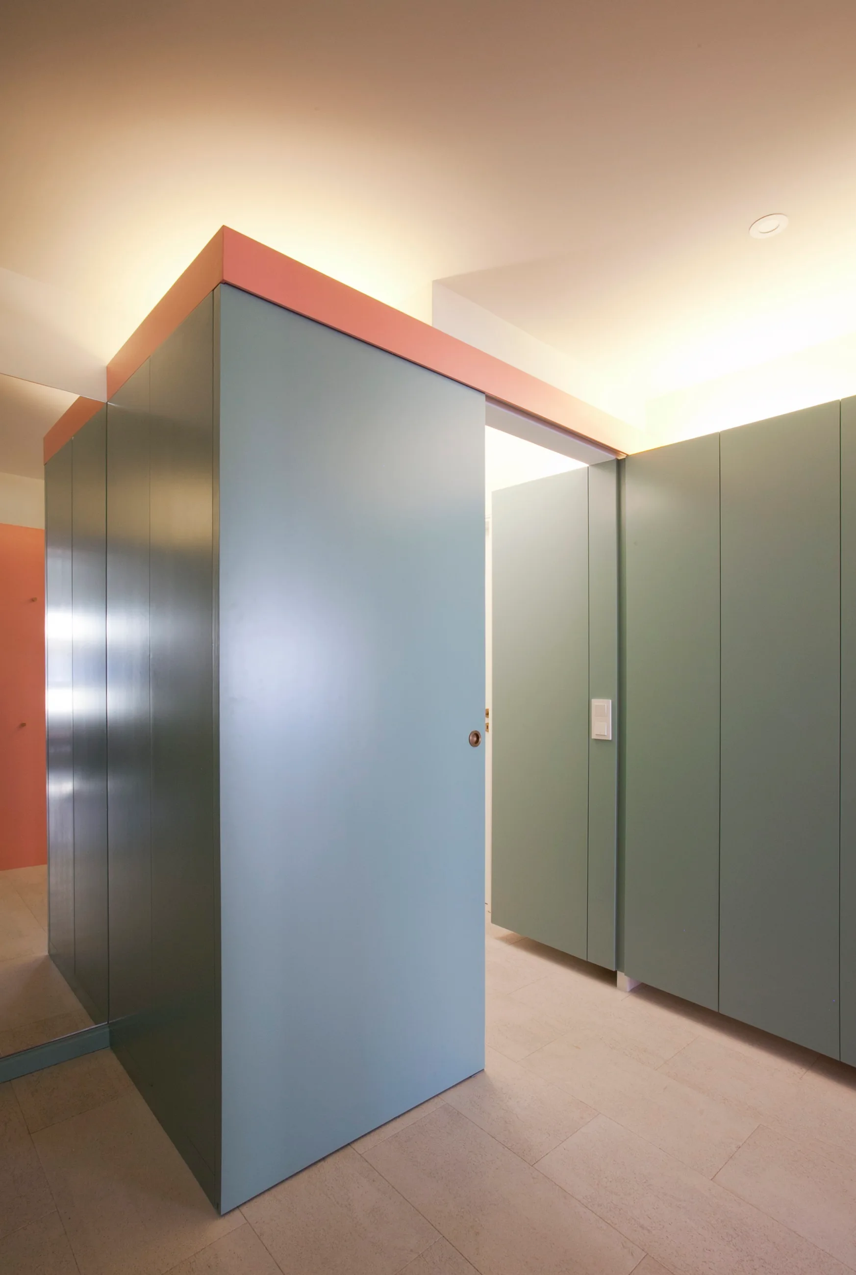 Sage green minimalist partition panels with a sliding door and a salmon pink trim stand below warm cove ceiling lighting.