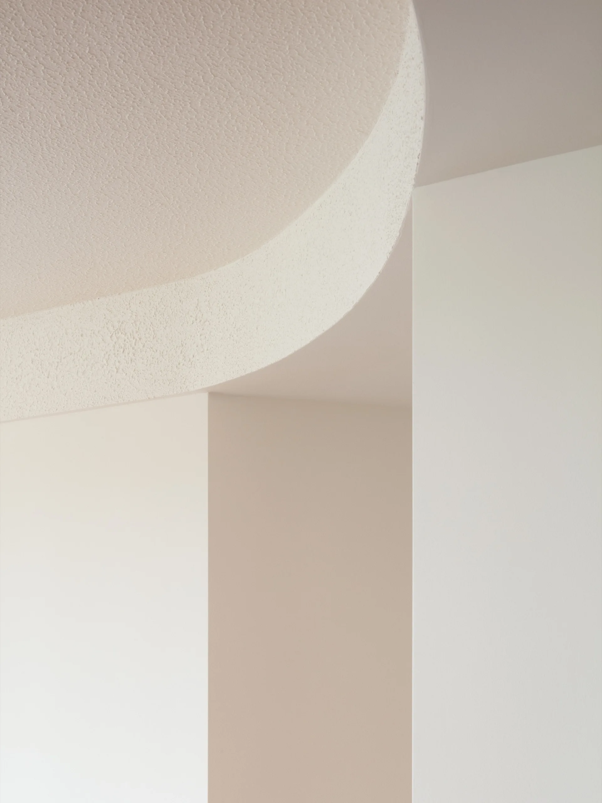 Architectural detail of a curved off-white ceiling with a stucco texture meeting smooth white interior walls.