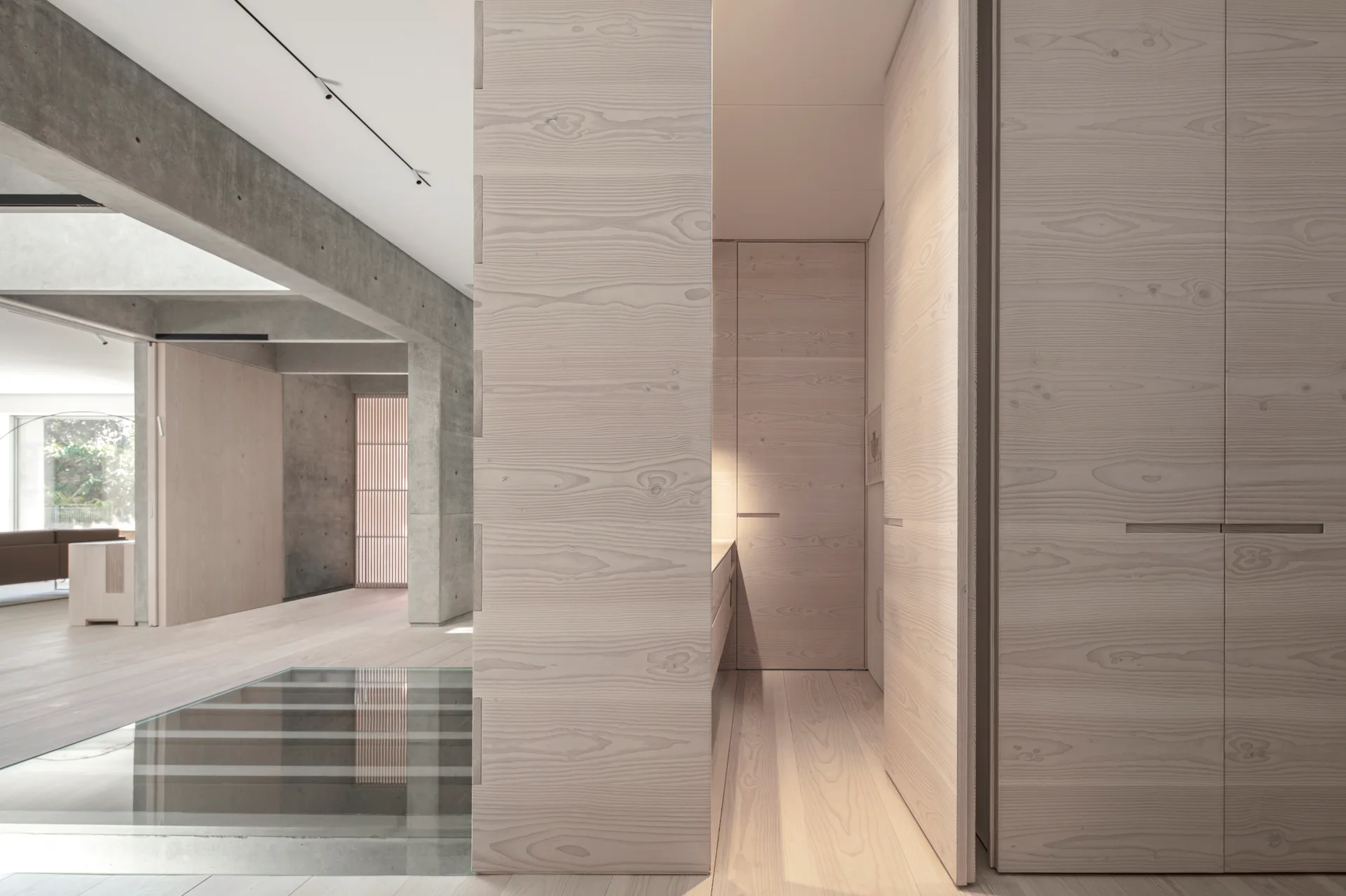 Minimalist hallway featuring light wood paneled walls, a matching wood floor, a glass floor insert, and exposed concrete structural beams overhead.