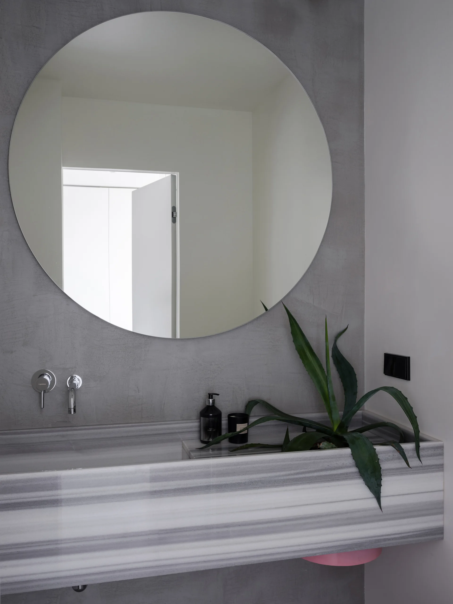 A large round mirror hangs on a textured gray wall above an integrated striped stone bathroom basin with a chrome faucet.