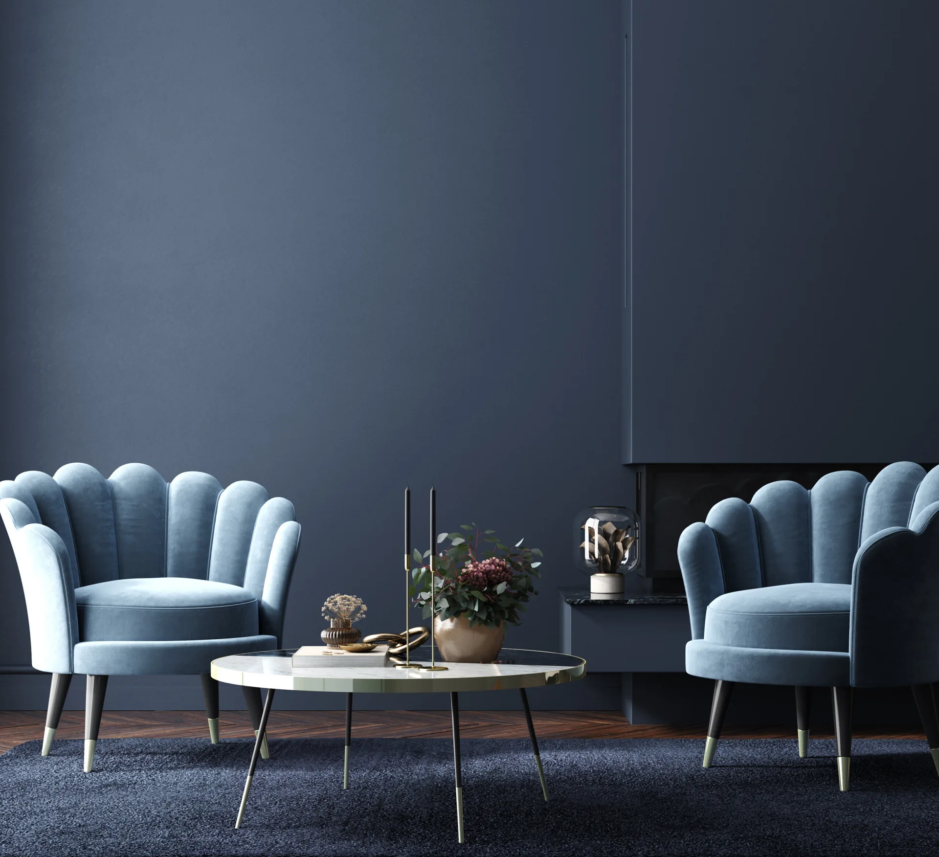 Two blue scalloped velvet armchairs face each other over a marble coffee table in a dark navy blue room.