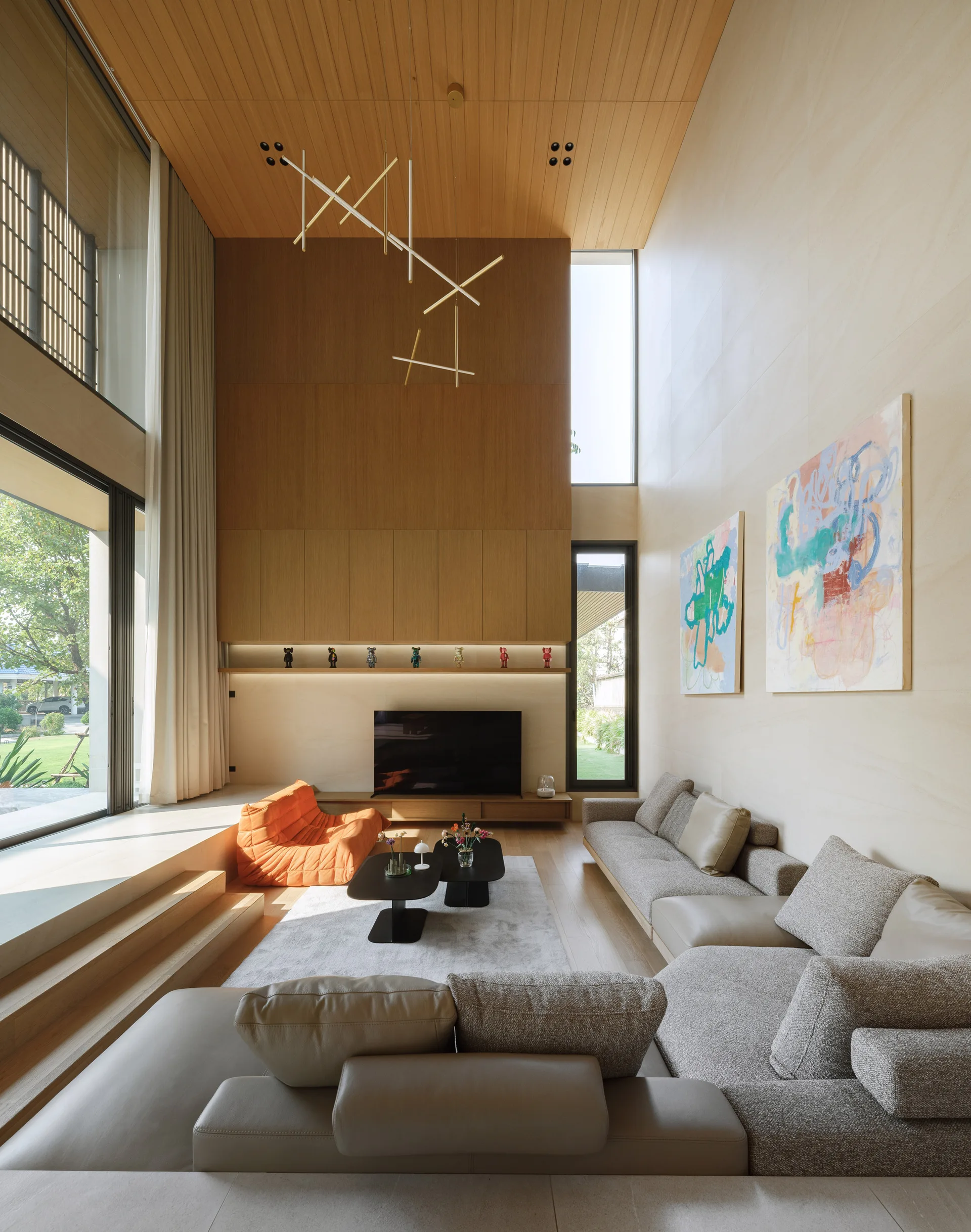 A sunken living room featuring a large grey sectional sofa, an orange accent chair, and double-height wood-paneled walls and ceiling.