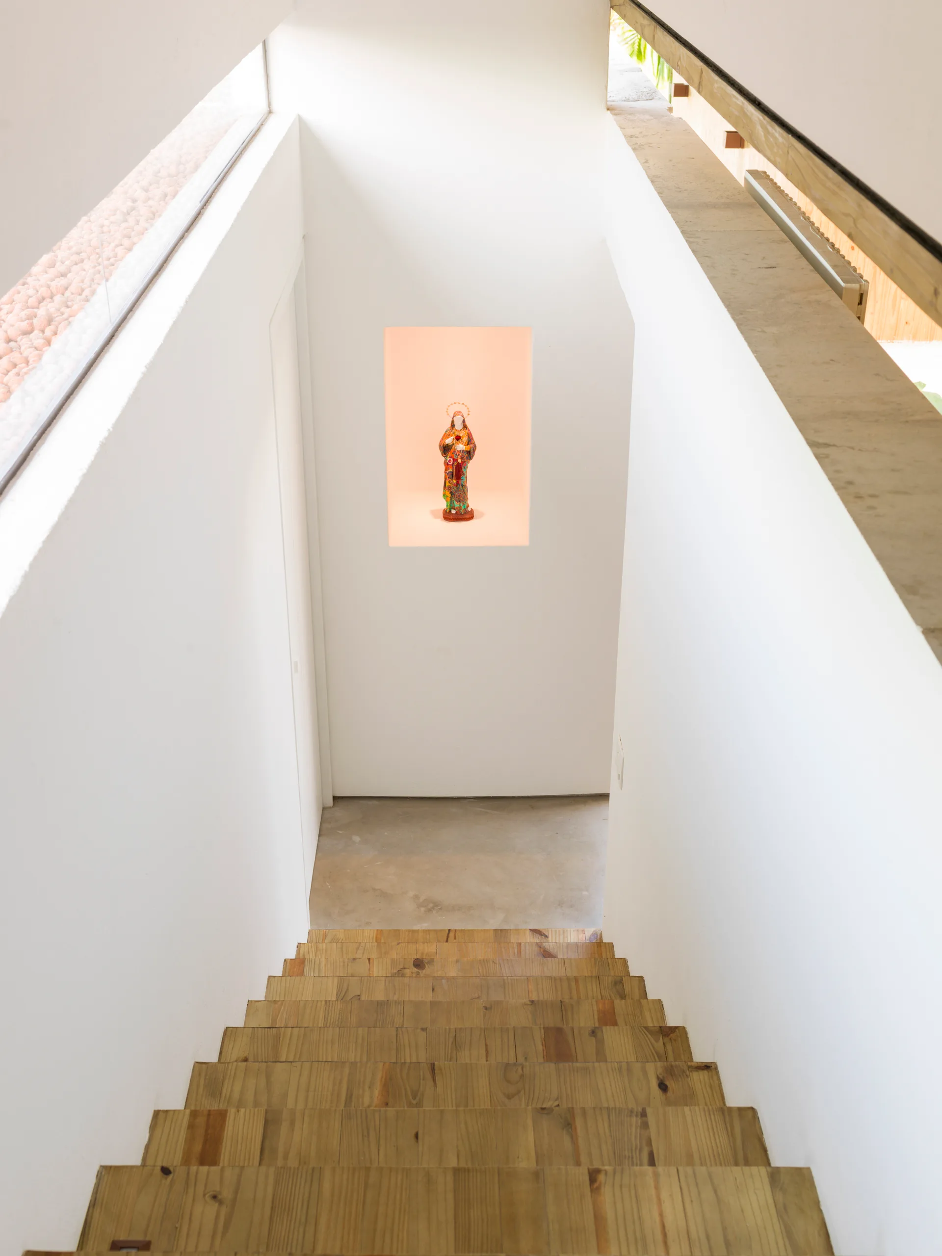 A top-down view of a wooden staircase leading to a white landing with a recessed wall niche containing a small figurine.