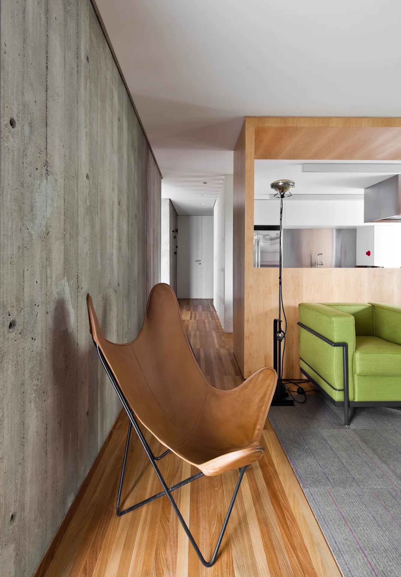 A modern room with a textured concrete wall, a tan leather butterfly chair, hardwood floors, and a bright green armchair.