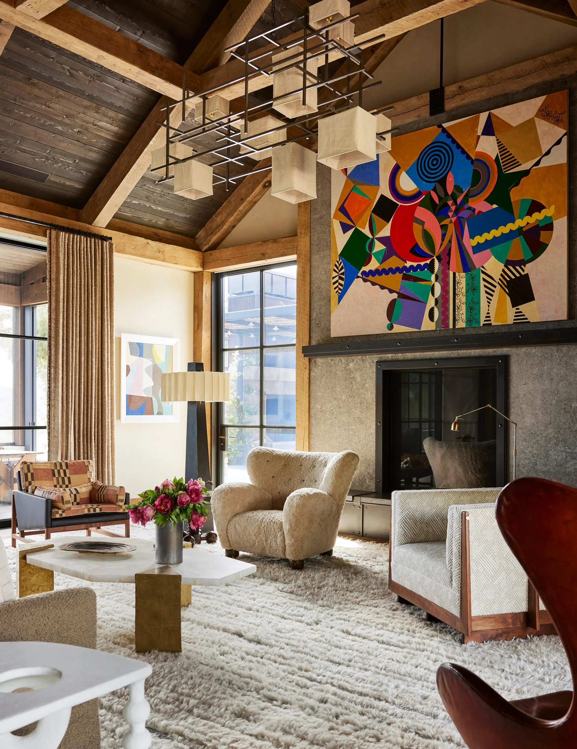A rustic living room featuring a vaulted wood ceiling, a stone fireplace with colorful abstract art, plush armchairs, and a thick shag rug.