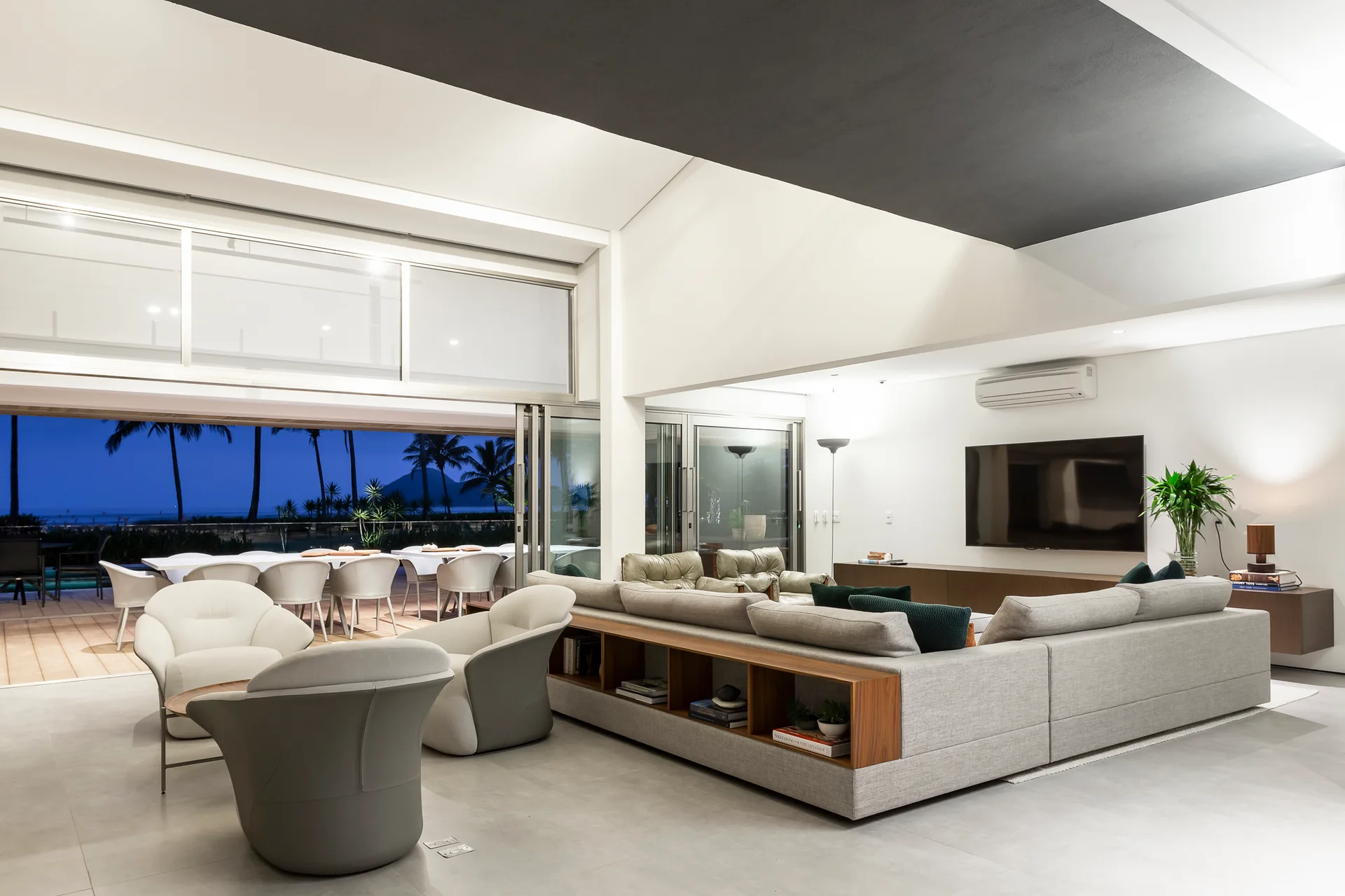 A grey sectional sofa with built-in wooden shelving sits in a modern living room next to large sliding glass doors opening to a patio.
