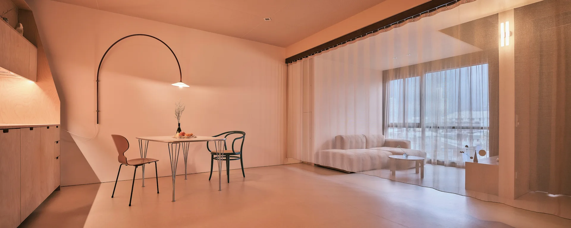 A warm peach-toned dining area with a wood cabinet and dining table next to a living space separated by a sheer white room divider.
