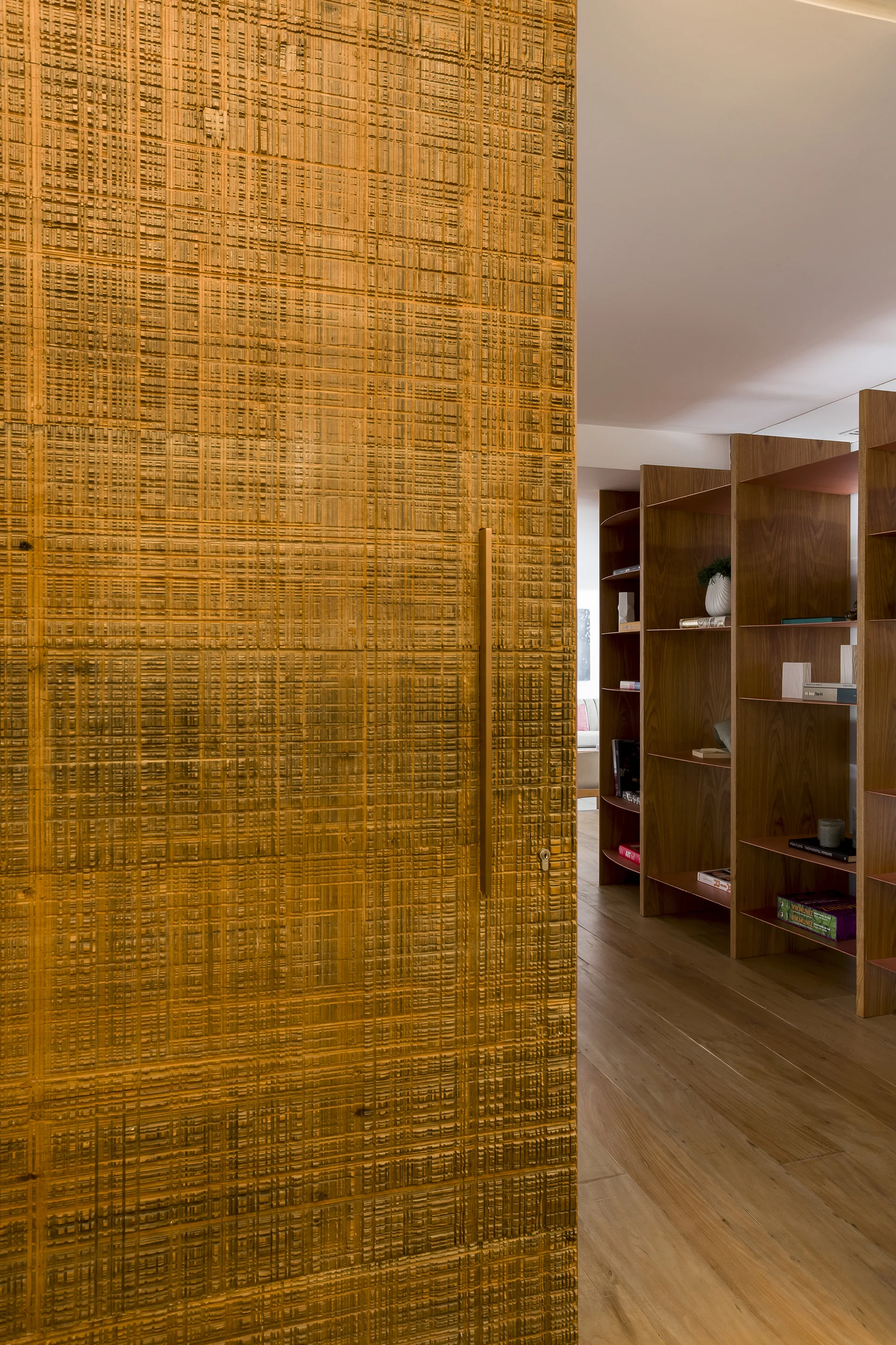A close-up of a carved wood door with a grid texture and a brass handle, opening to a hallway with wooden open shelving.