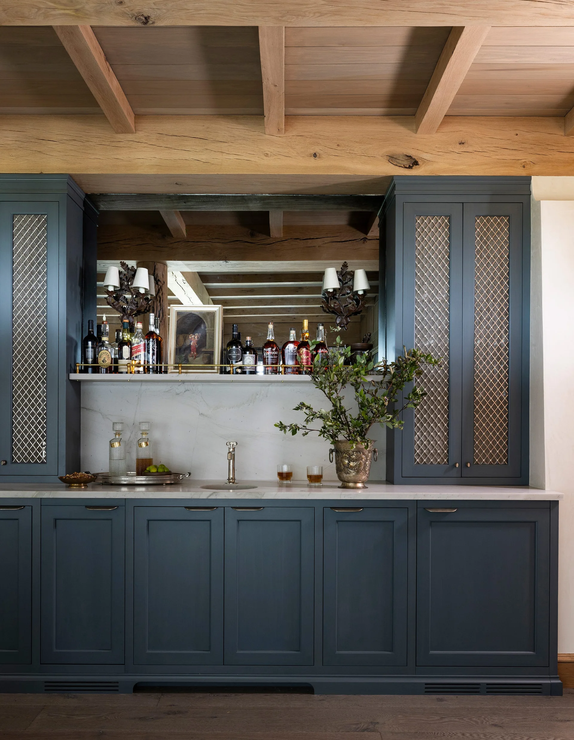 A navy blue built-in home bar features a white stone countertop, a mirrored backsplash, and upper cabinets with decorative metal latticework doors.