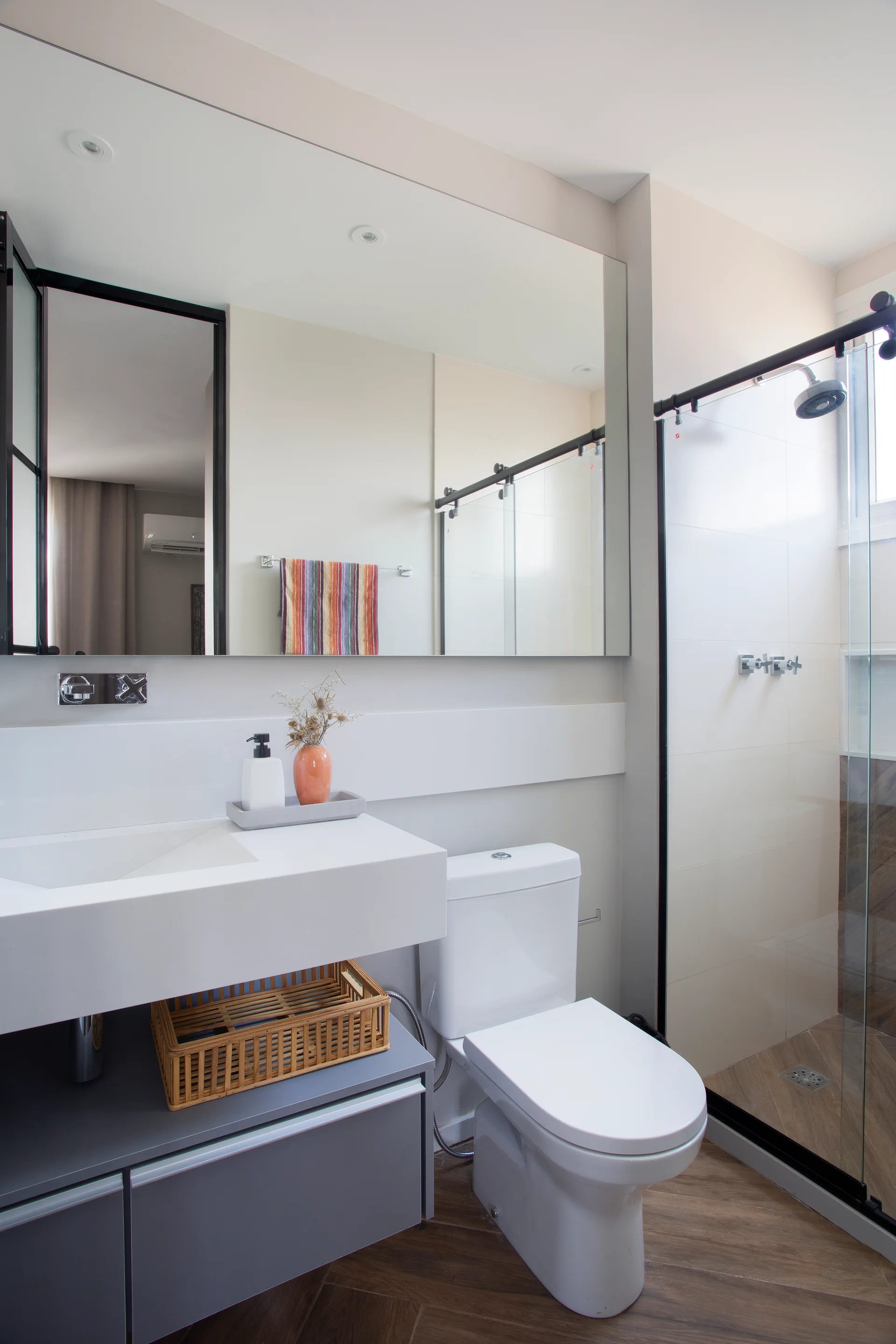 A modern bathroom featuring a white floating vanity, a gray lower cabinet, a toilet, and a glass shower with herringbone wood-look tiles.