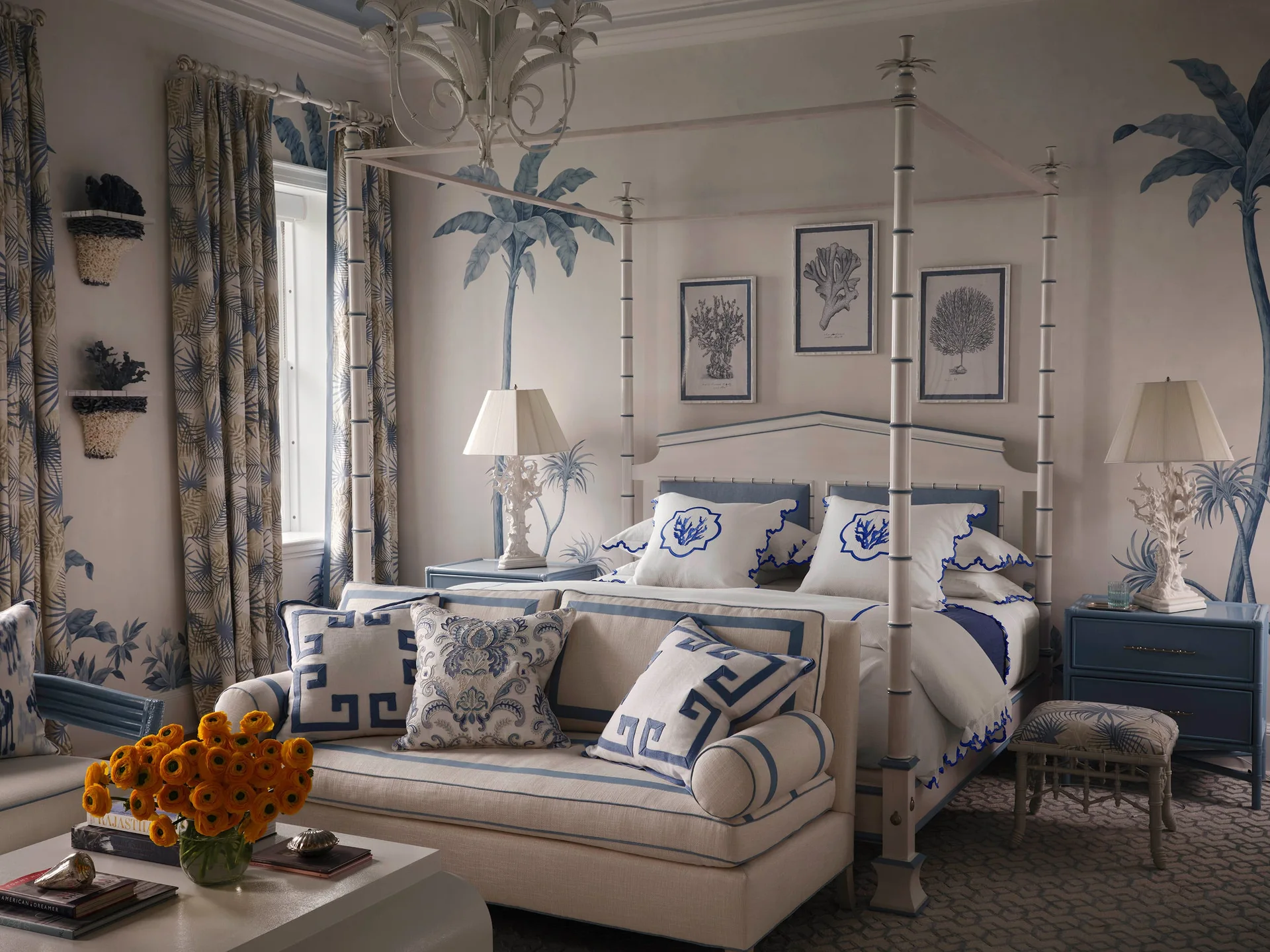 A coastal bedroom featuring a four-poster bed, blue palm tree wall mural, lacquered nightstands, and a coordinating sofa at the foot of the bed.