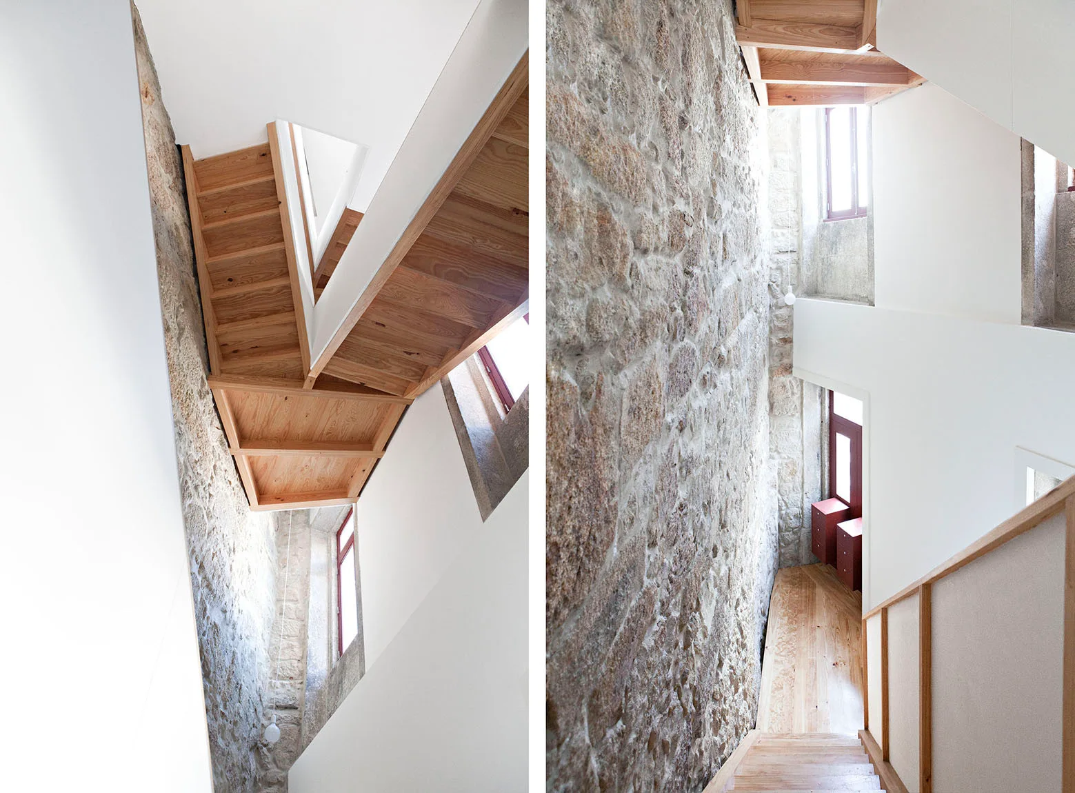 A modern wooden staircase with light wood treads climbs alongside a tall rough exposed stone wall and smooth white plaster walls.