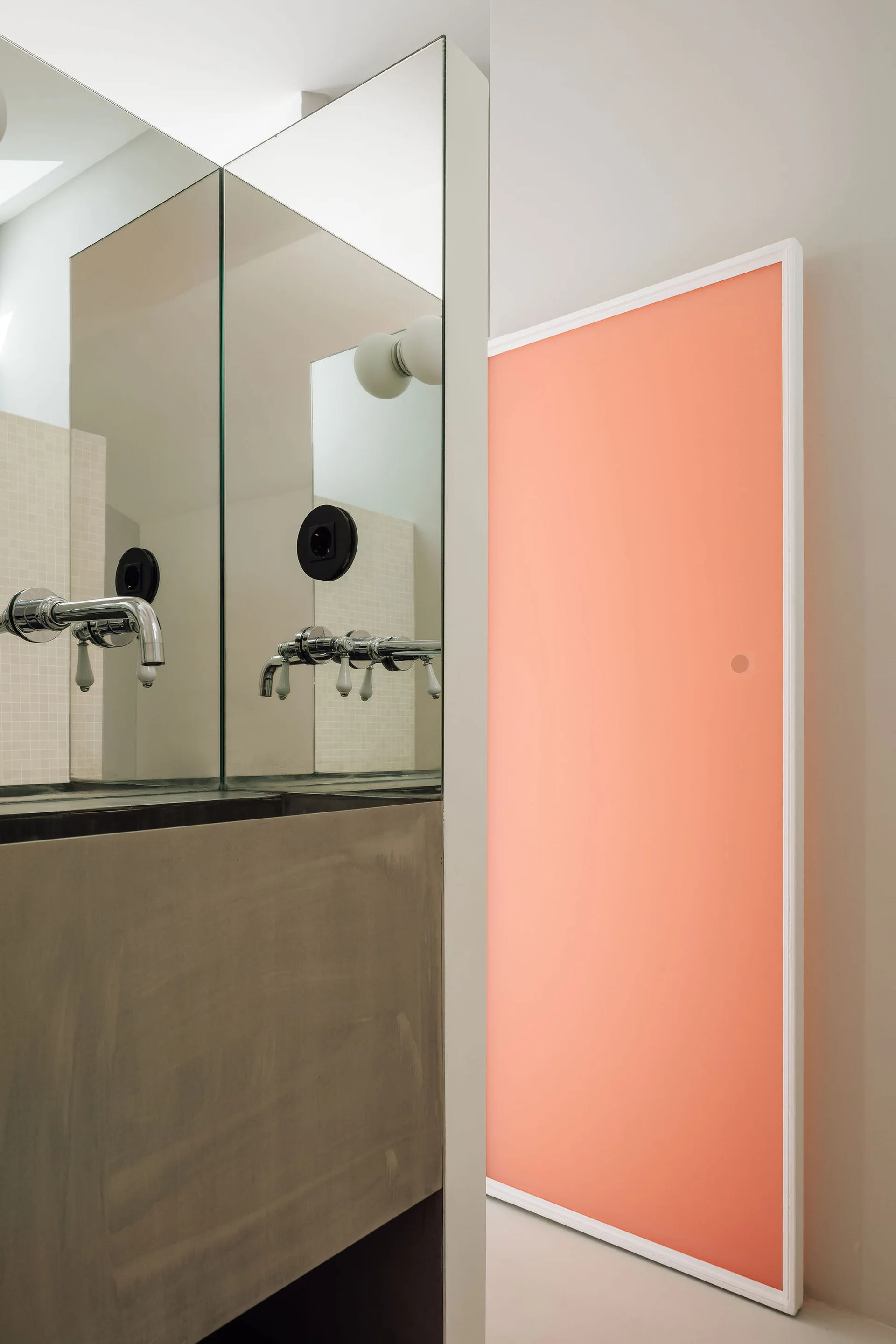 A modern bathroom vanity area with a concrete basin, wall-mounted chrome faucet, large mirror, and a bright coral pink sliding door.