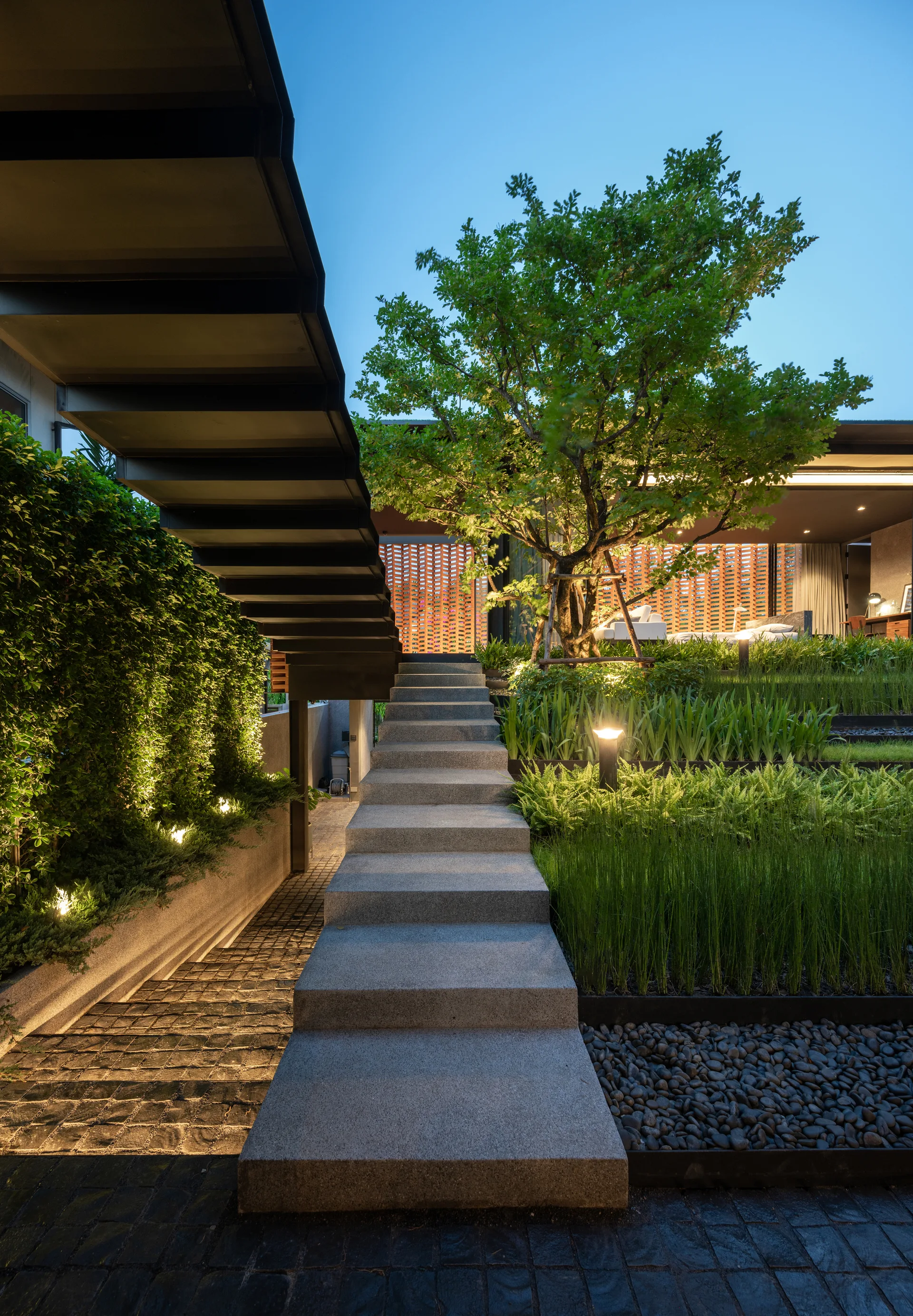 A central stone staircase leads up through terraced green plantings with warm accent lighting under a dark overhead canopy at dusk.