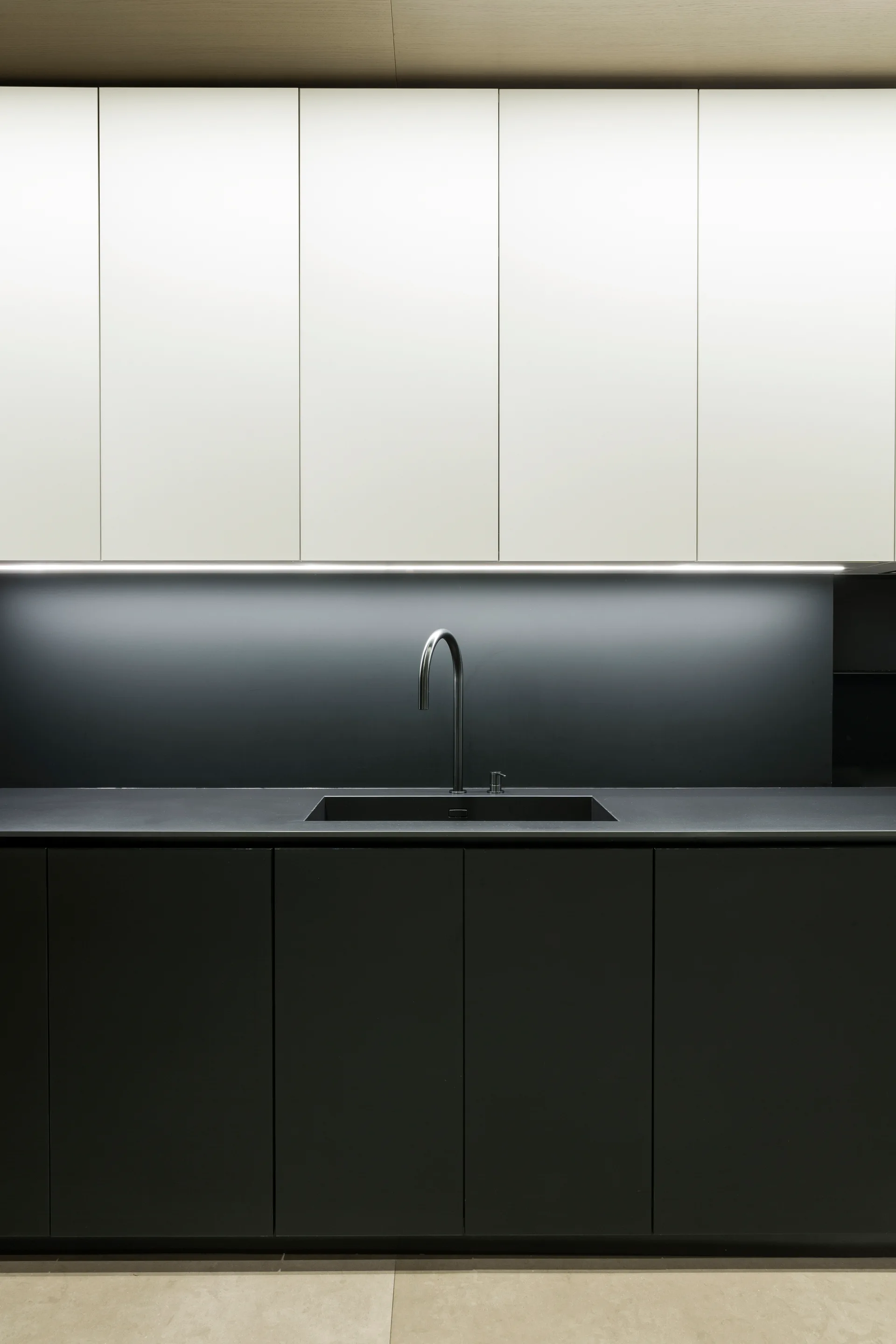 Minimalist kitchen featuring flat-front white upper cabinets, matte black lower cabinets, a built-in black sink, and integrated LED lighting.
