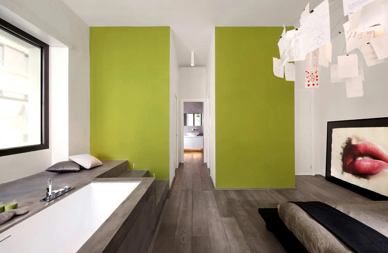 A modern bedroom suite featuring a built-in grey bathtub on a platform, vibrant lime green walls, wood plank floors, and a low platform bed.