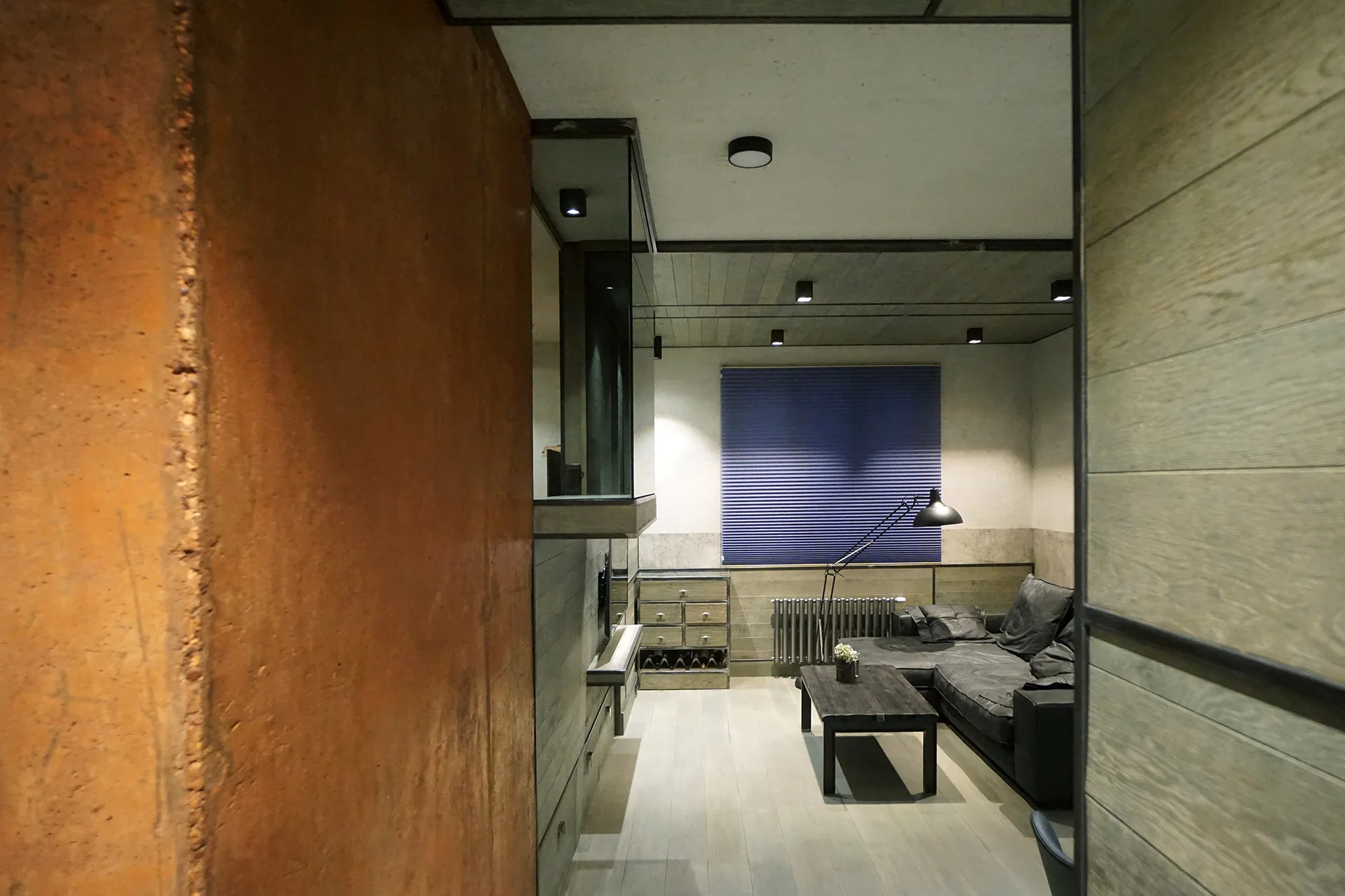A moody industrial living room features a rust-colored accent wall, a dark gray sectional sofa, and horizontal wood-plank paneling.
